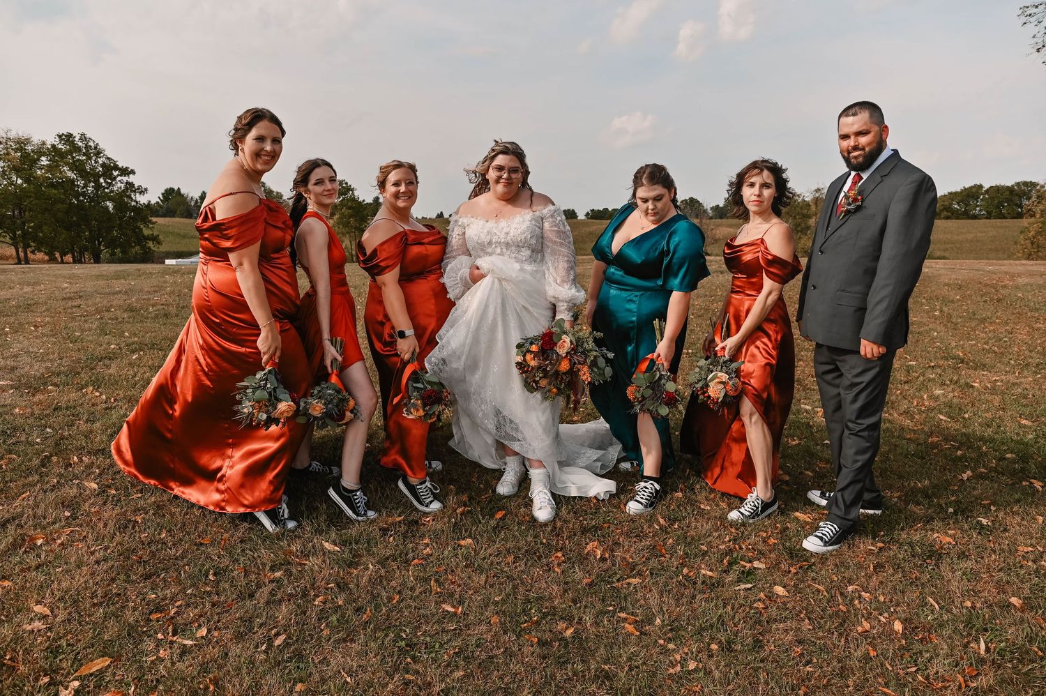 Wedding party sitting together on grass during fall outdoor photoshoot.