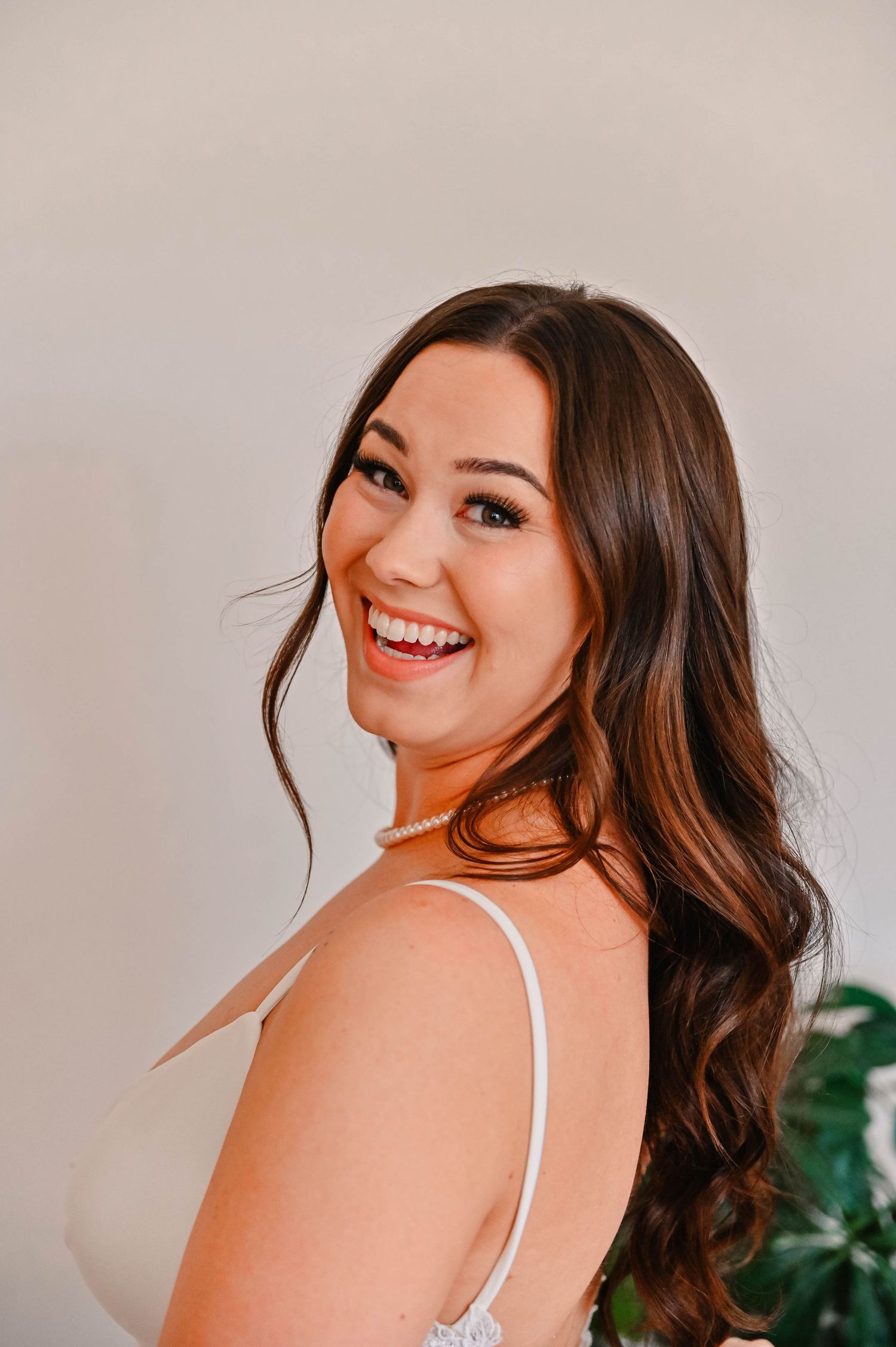 Woman in white top poses against light background with flowing brown hair.
