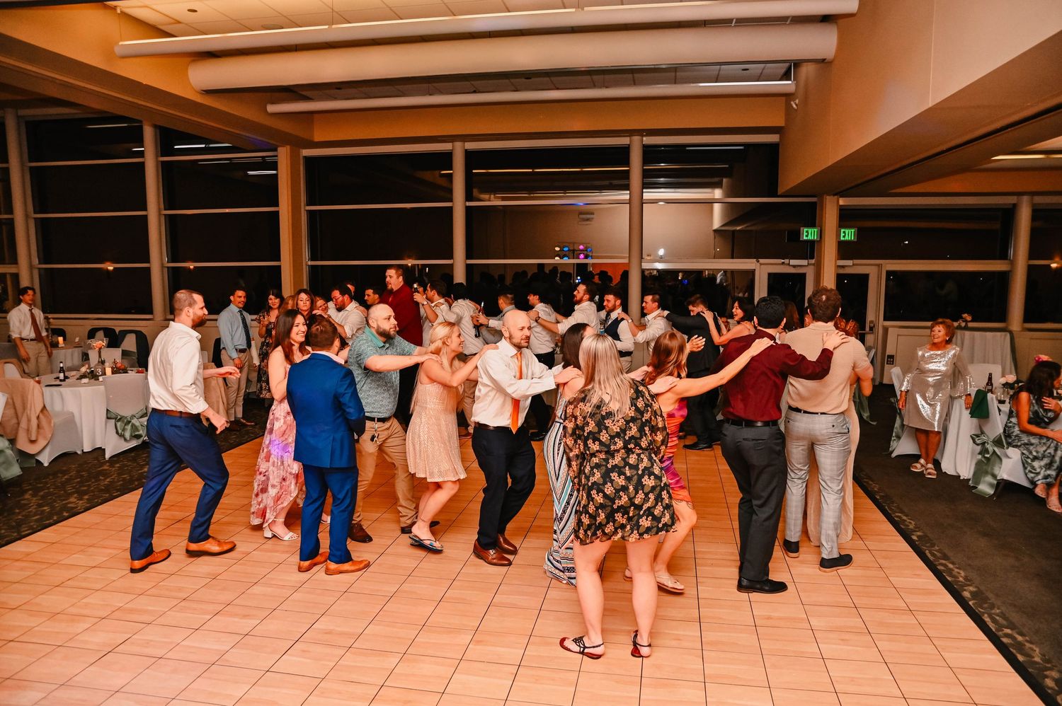 Wedding guests dance and socialize on a tiled floor at an indoor reception venue.