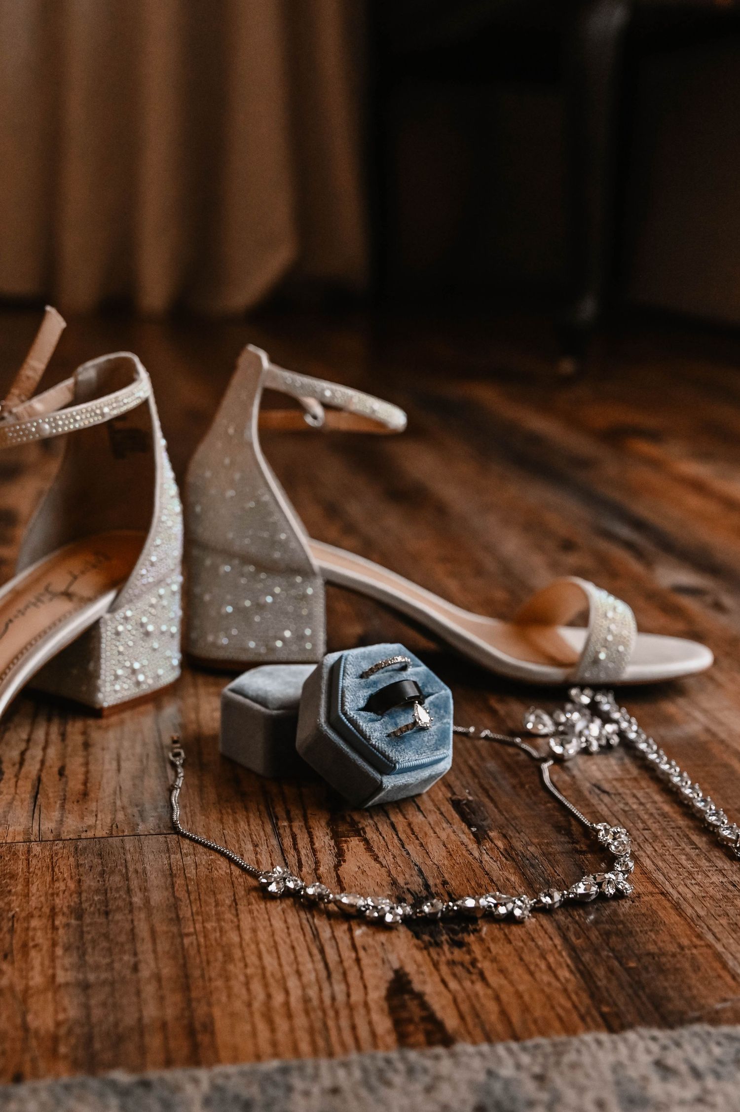 Wedding accessories including sparkly heels and jewelry on rustic wooden floor.