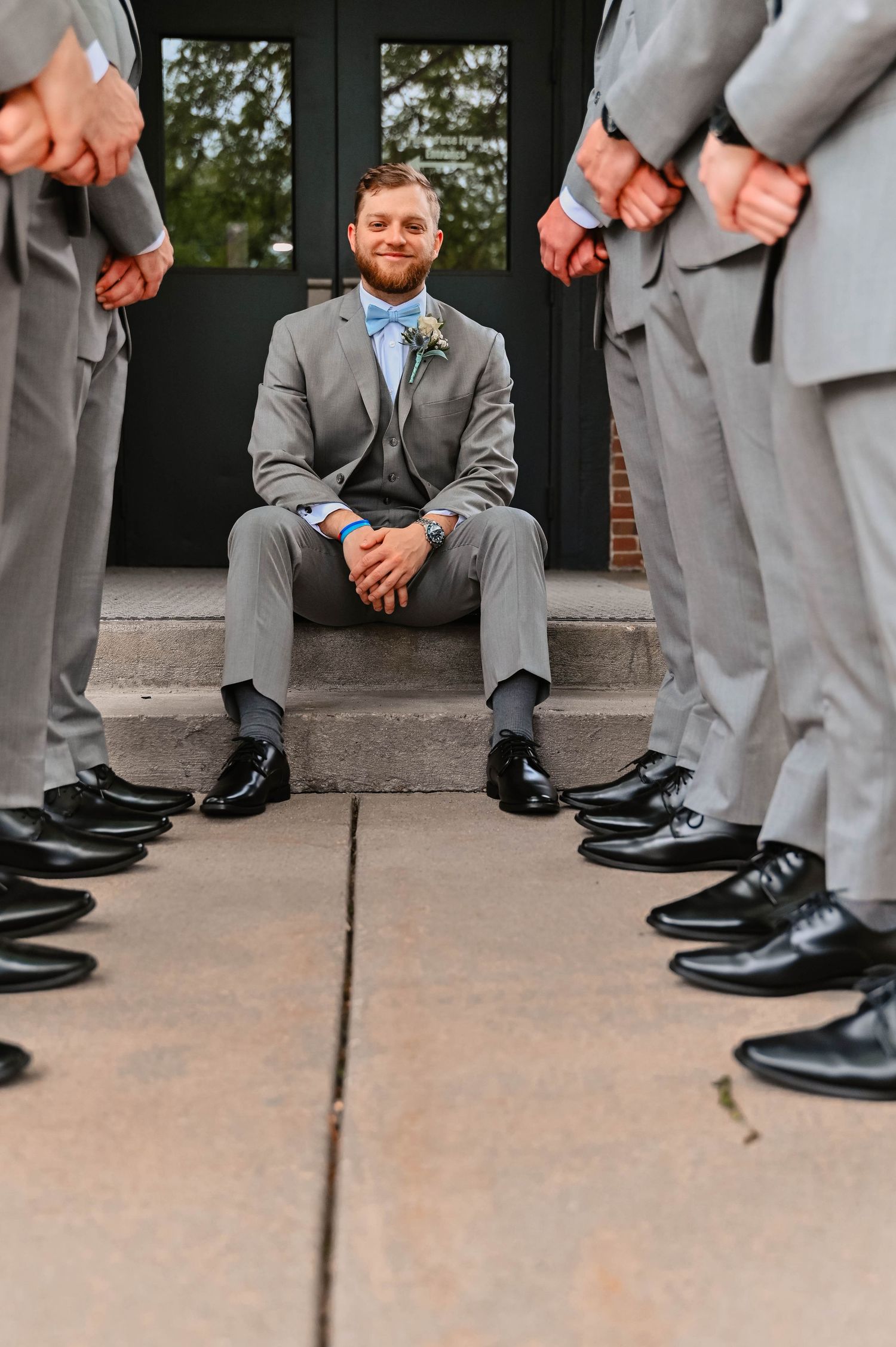 Groomsmen in gray suits showing off their polished black dress shoes while standing on concrete.