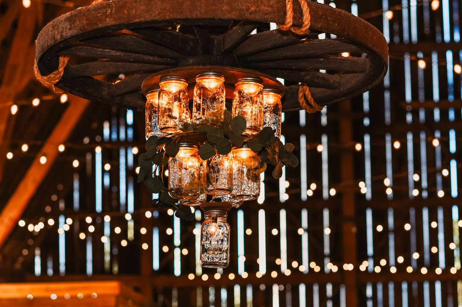 Rustic barn venue interior with hanging crystal chandeliers and string lights creating romantic ambiance.