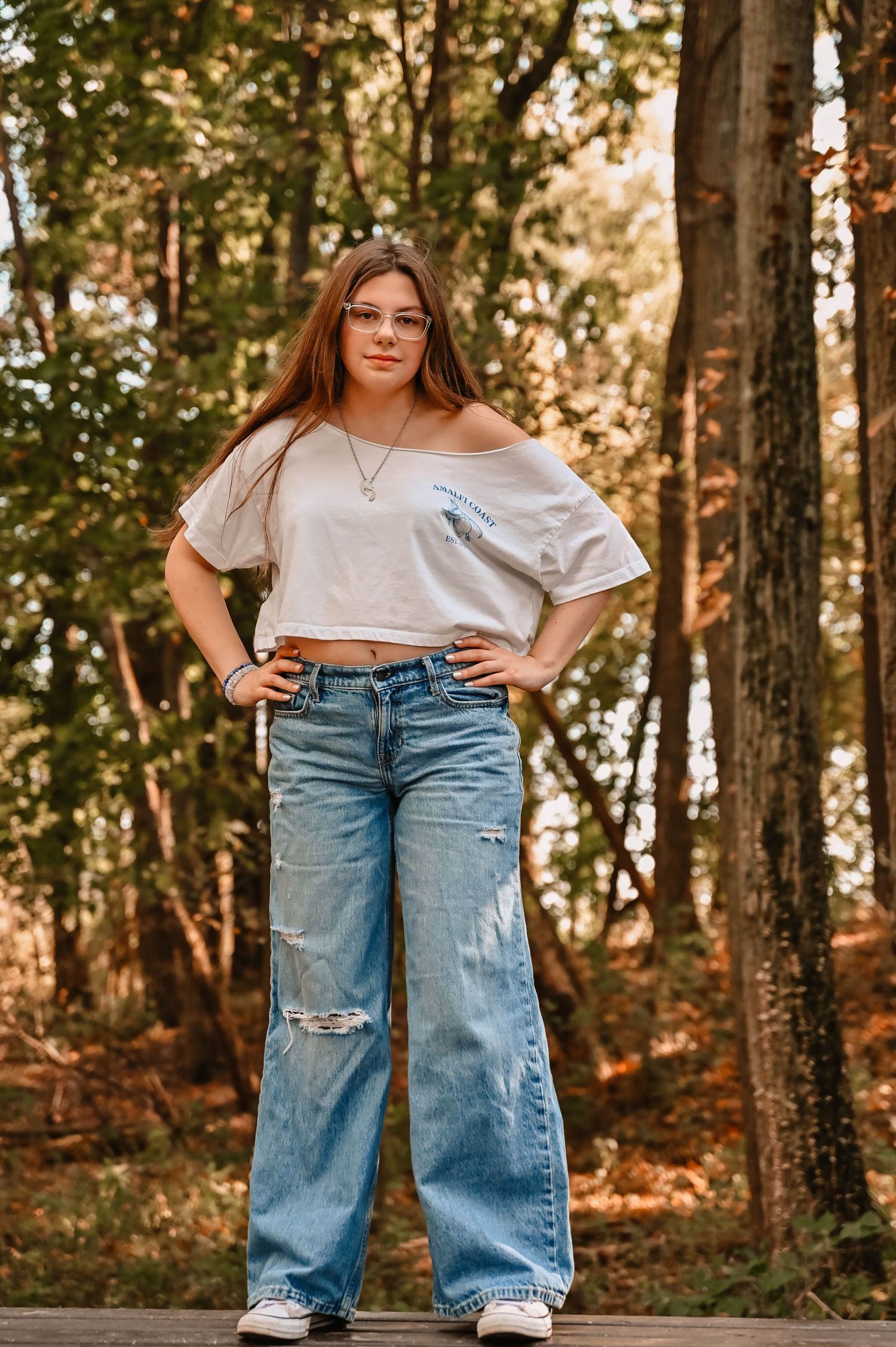 Casual fashion photography showcasing distressed denim and white tops in a wooded setting.