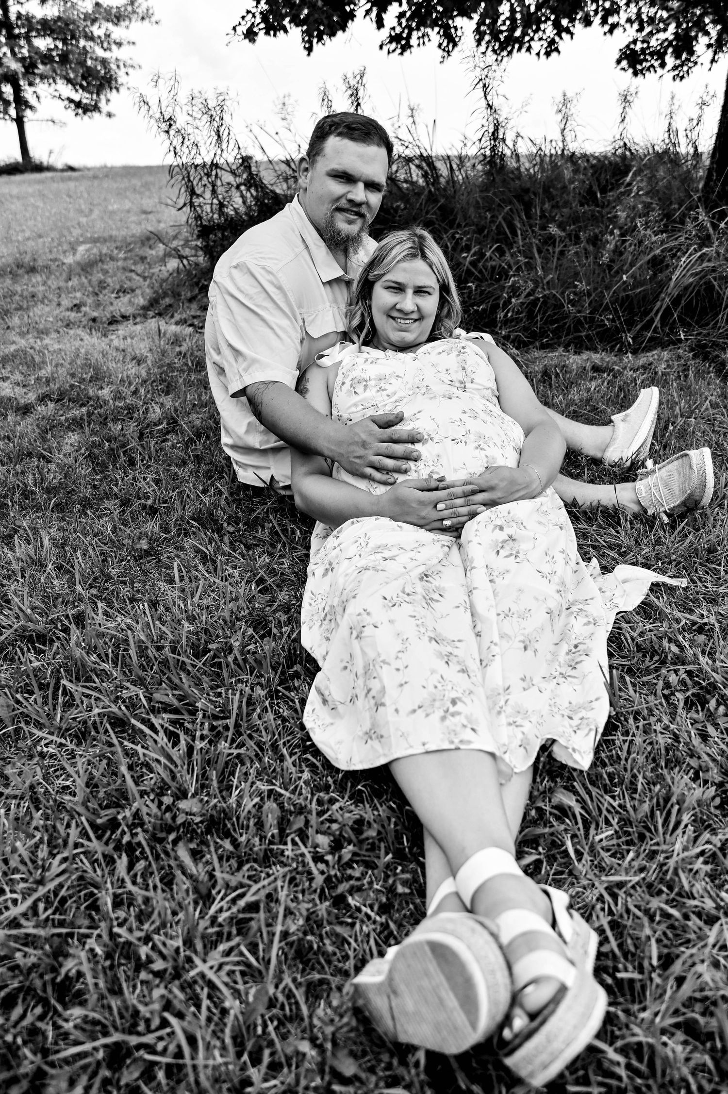 Black and white photo of couple lounging on grass during maternity session.