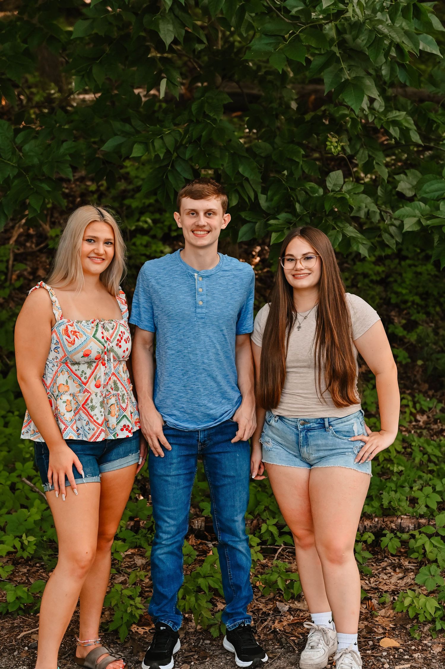 A group poses together in casual summer outfits against a leafy green backdrop.