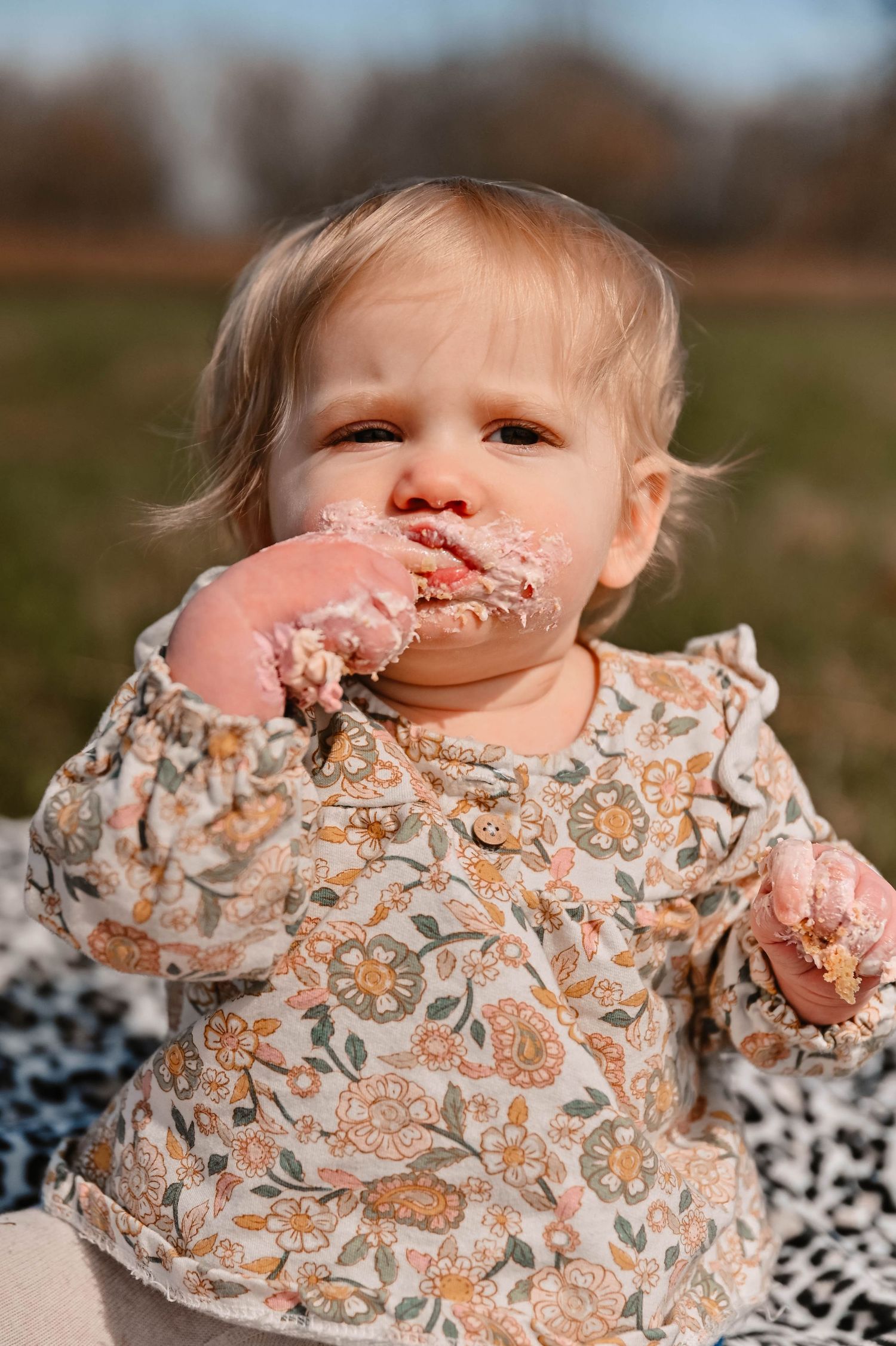 Baby in floral dress plays and smiles during outdoor photo session.
