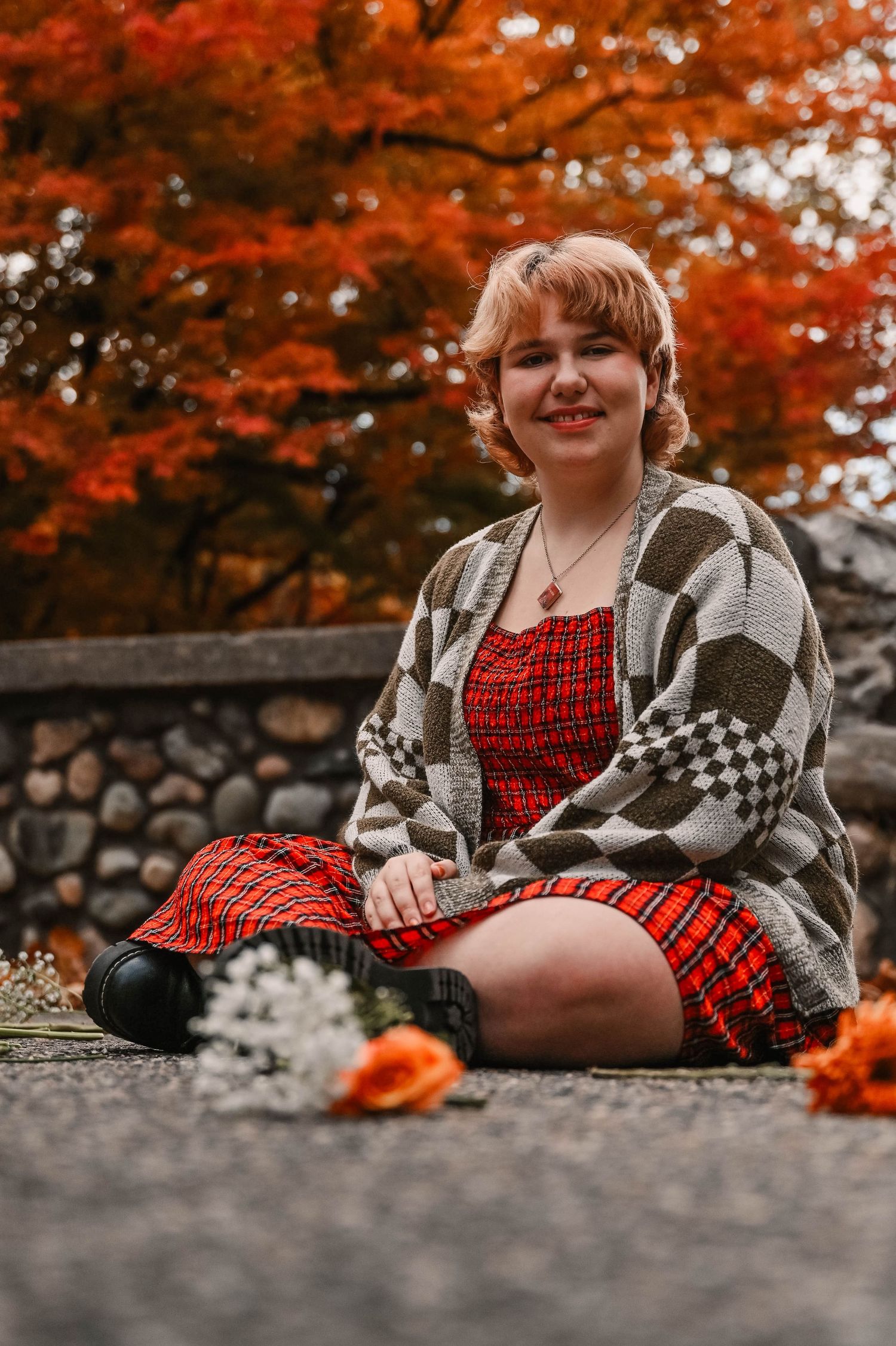Autumn portrait on stone wall wearing red dress and checkered cardigan.