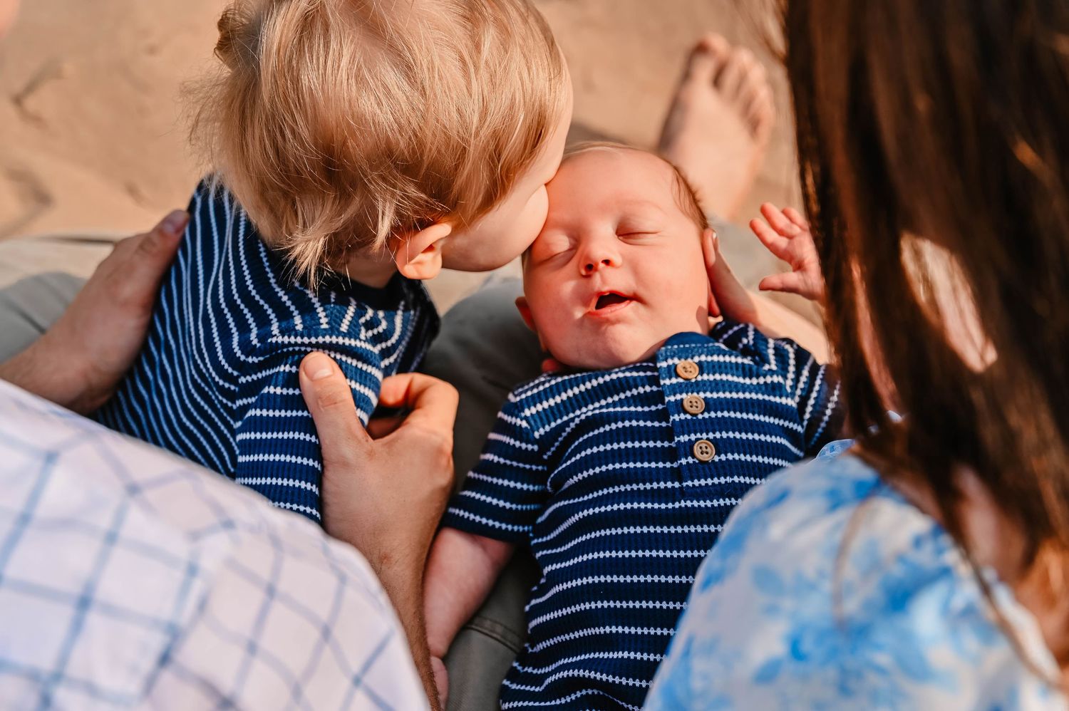 Baby in striped outfit being held and cuddled outdoors.