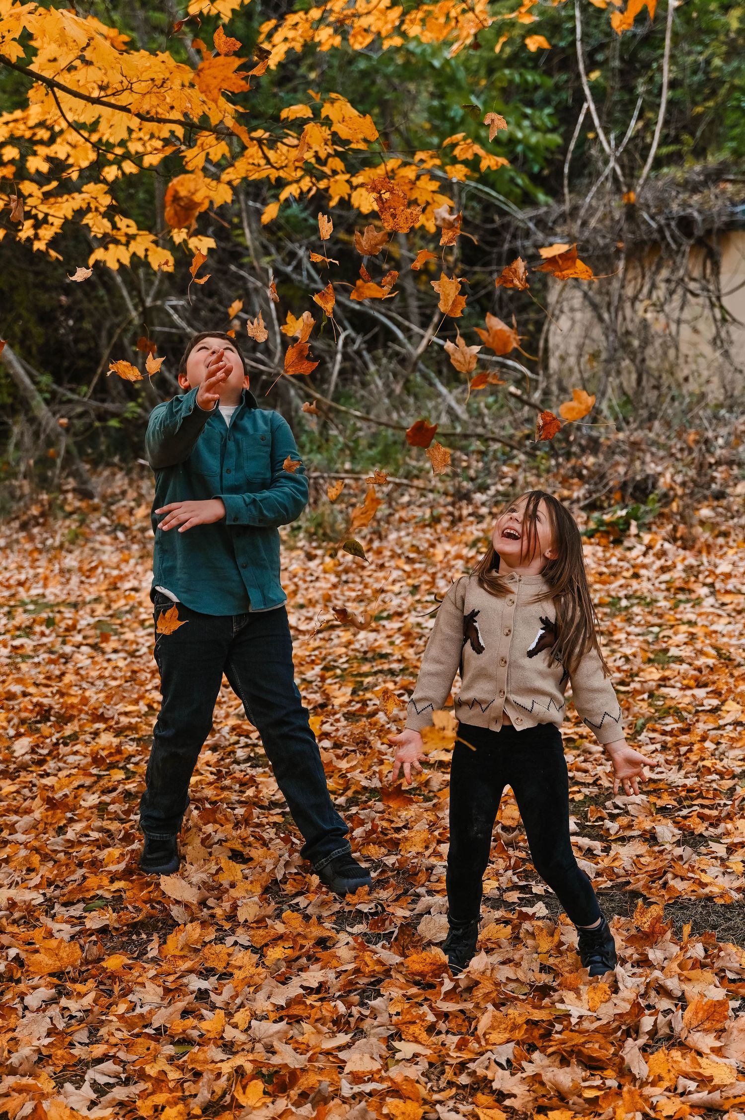 Children playing in fallen autumn leaves under bright orange foliage.