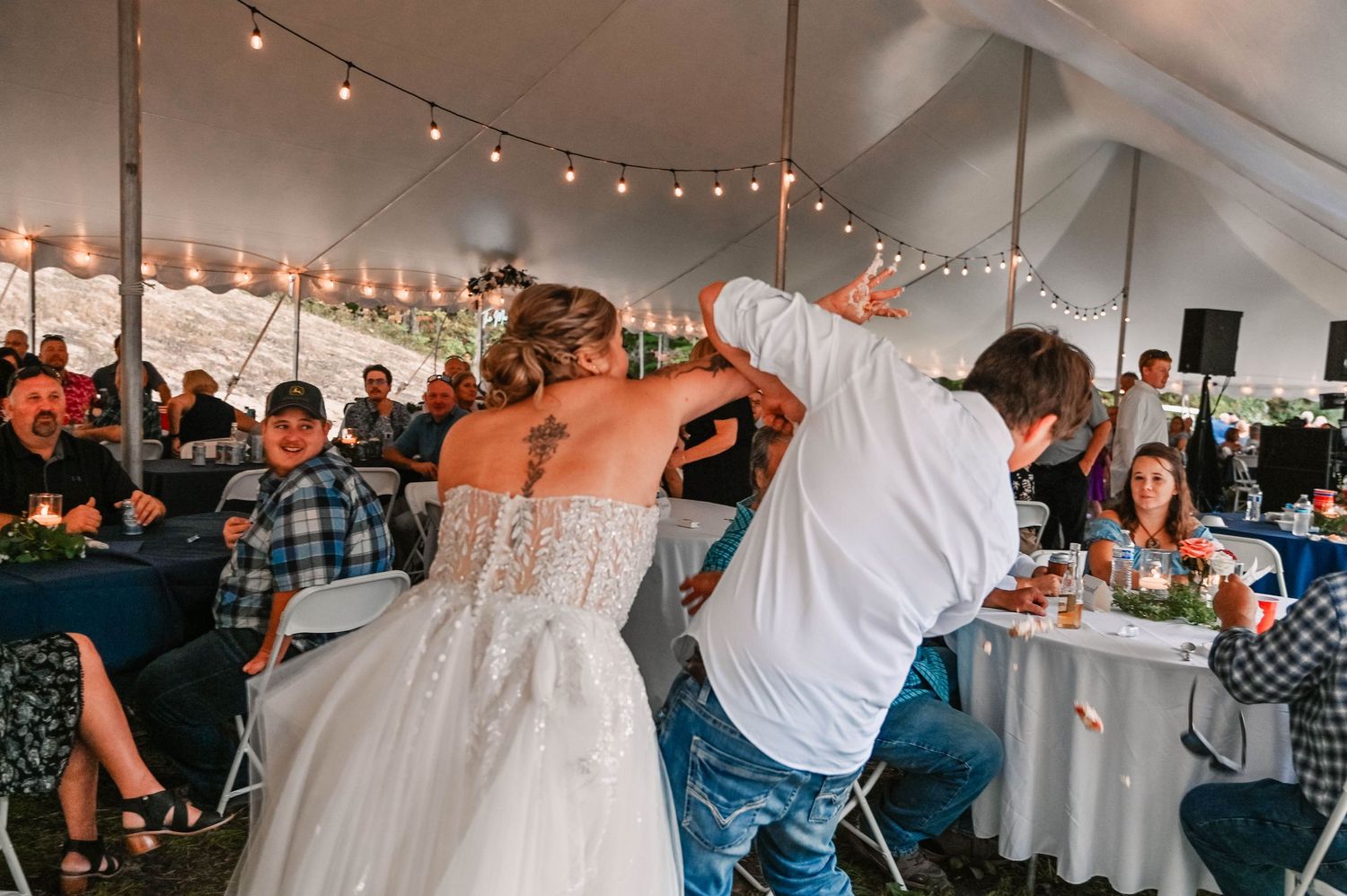 Wedding reception celebration under a white tent with string lights and dancing guests.