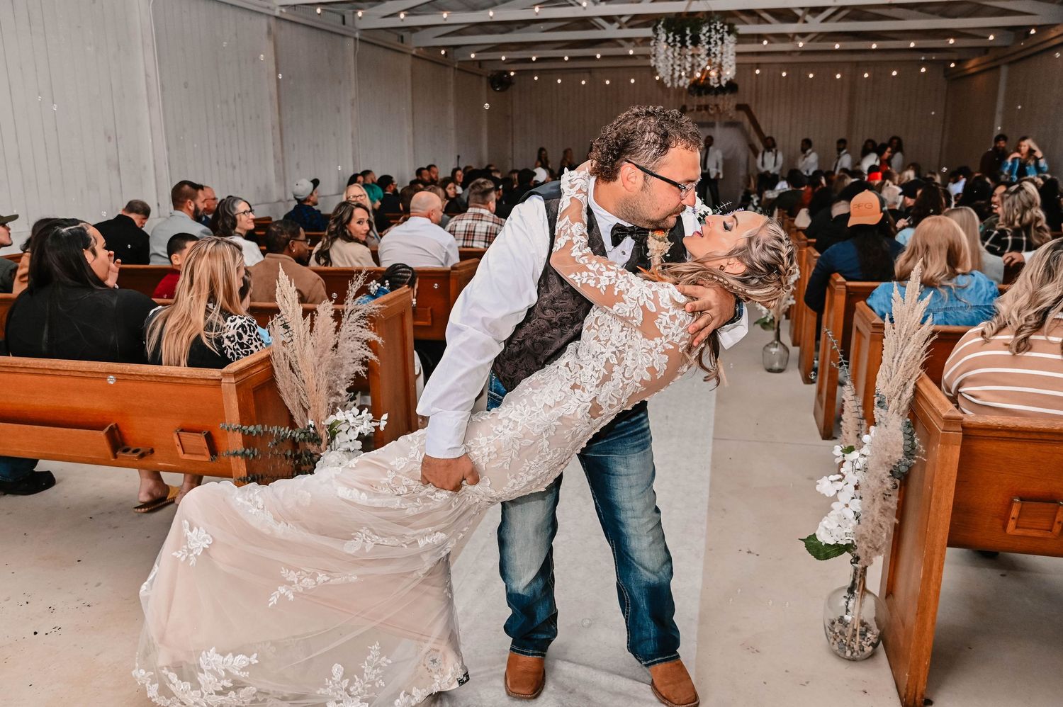 Wedding couple and guests dancing joyfully at a reception with string lights overhead.