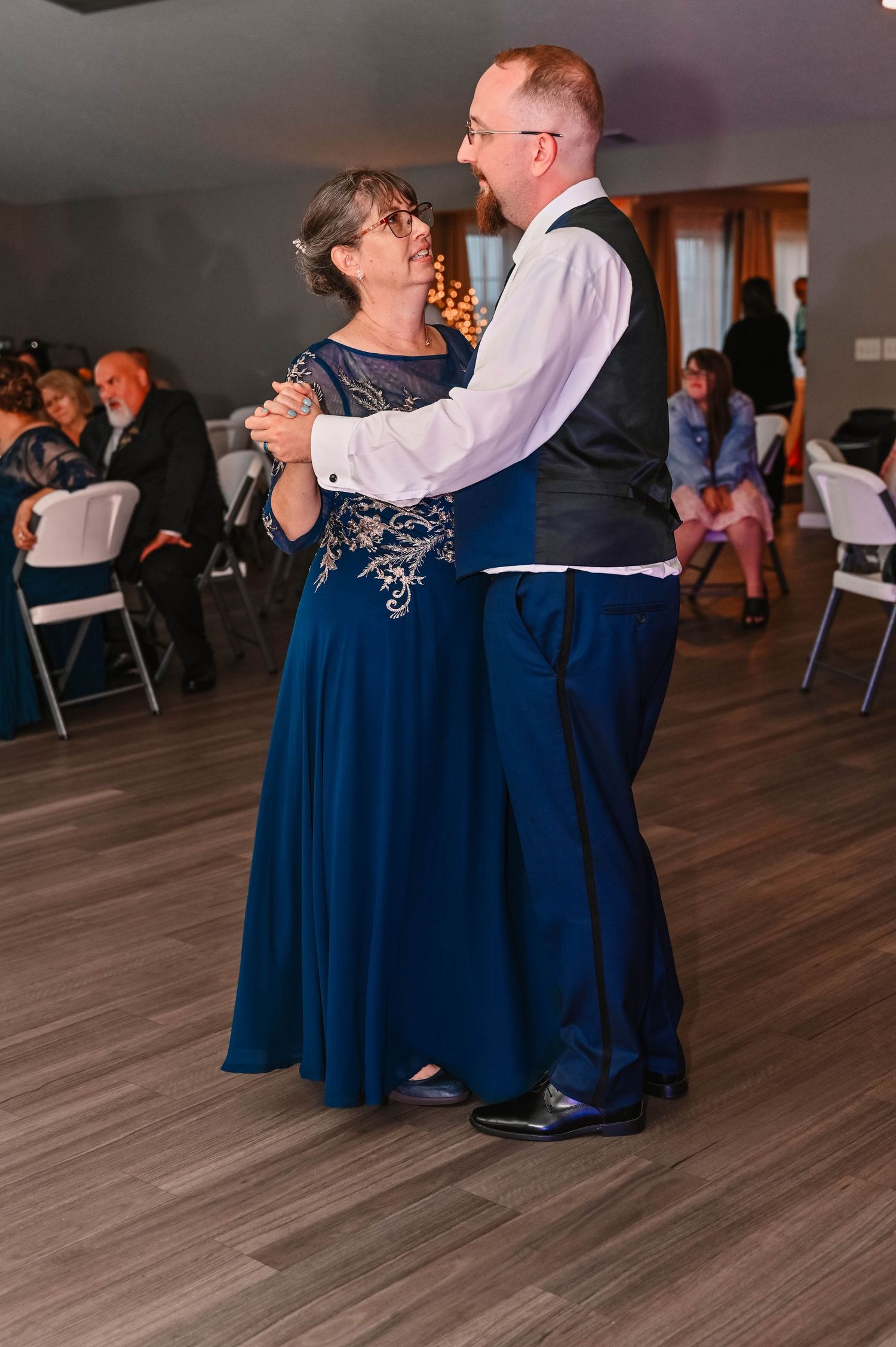 Couples dancing on wooden floor at wedding reception in evening lighting.