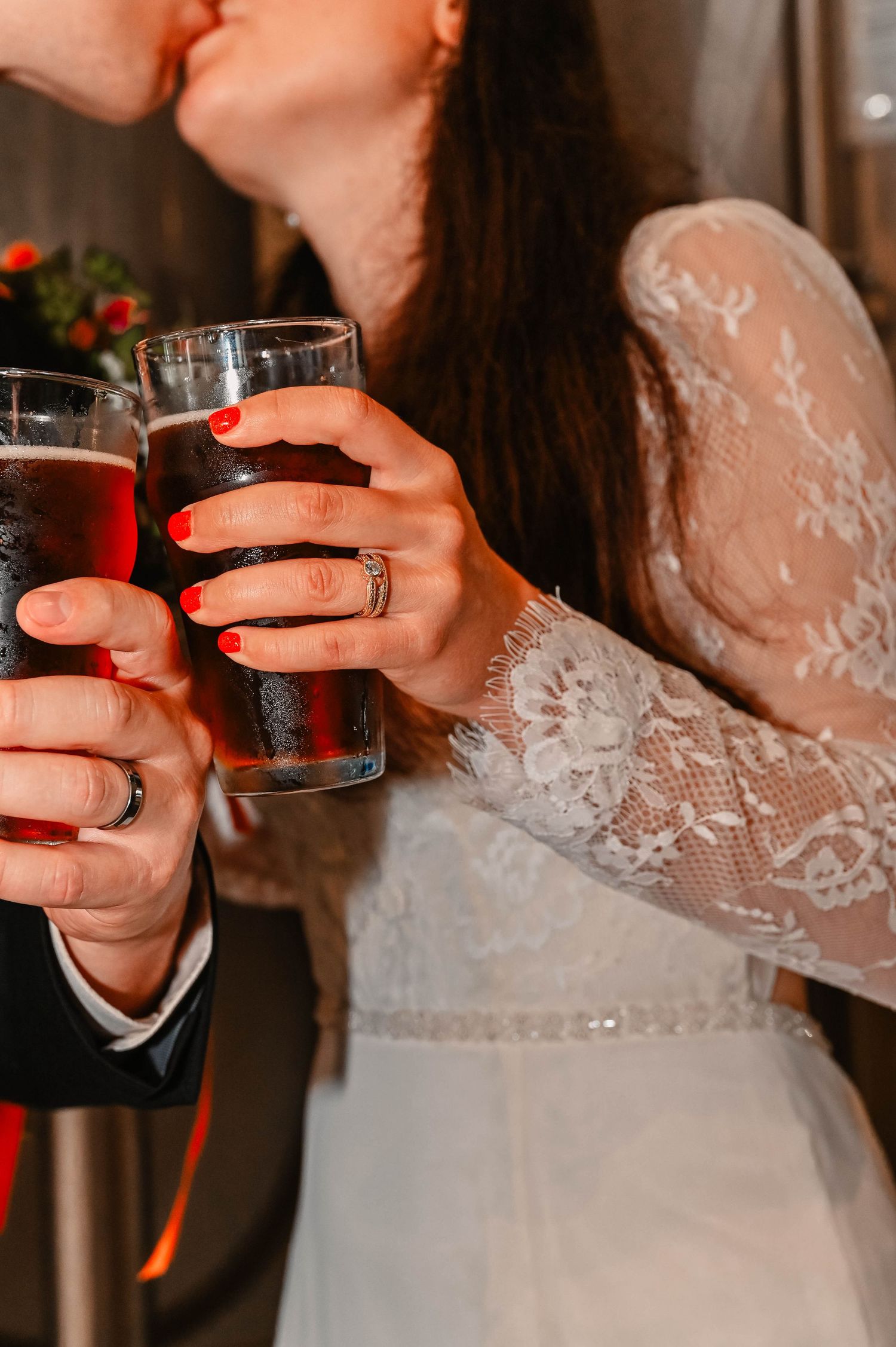 Close-up of couple toasting with dark drinks while showing off wedding rings.