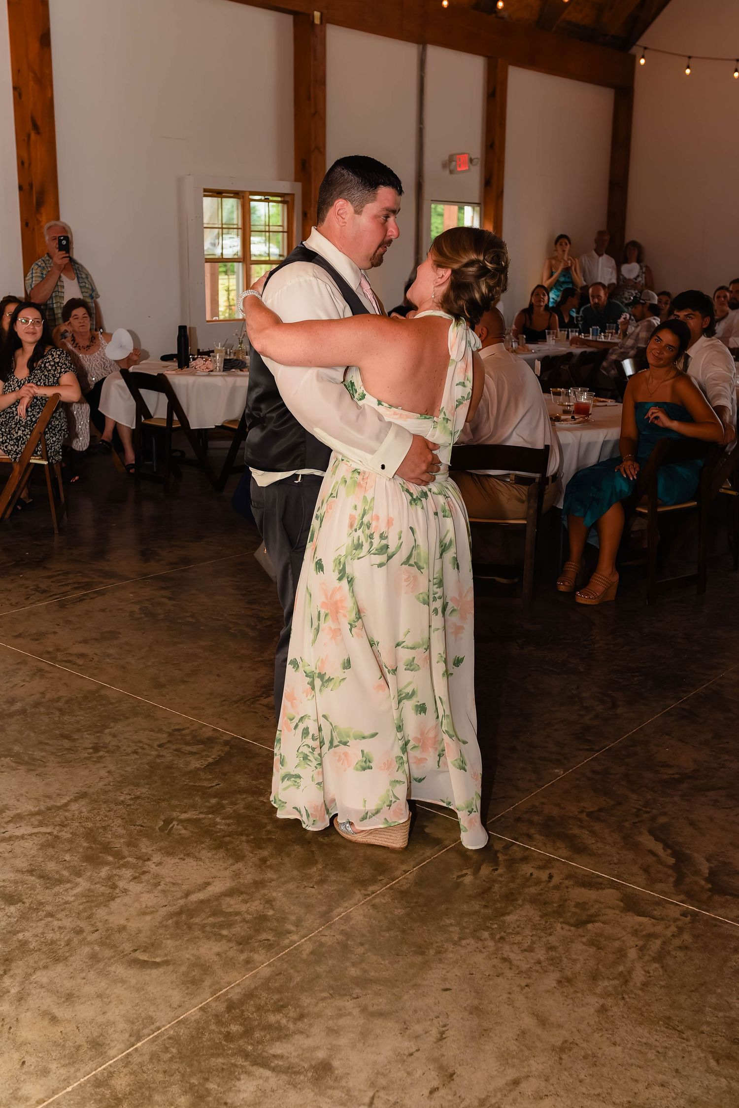 Wedding couple dances together in a rustic reception venue with string lights.