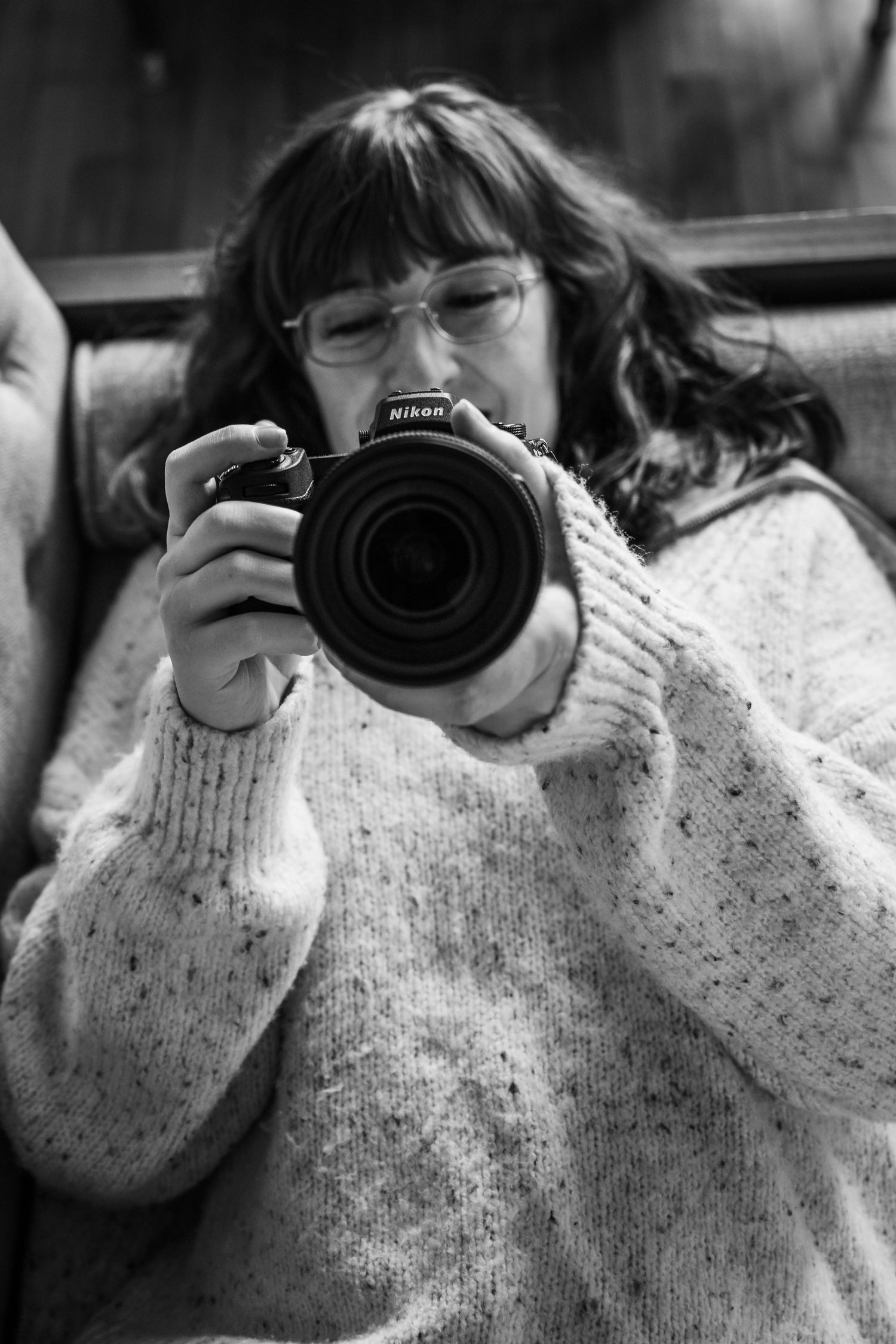 A series of black and white photos showing someone wearing a sweater holding a camera lens.