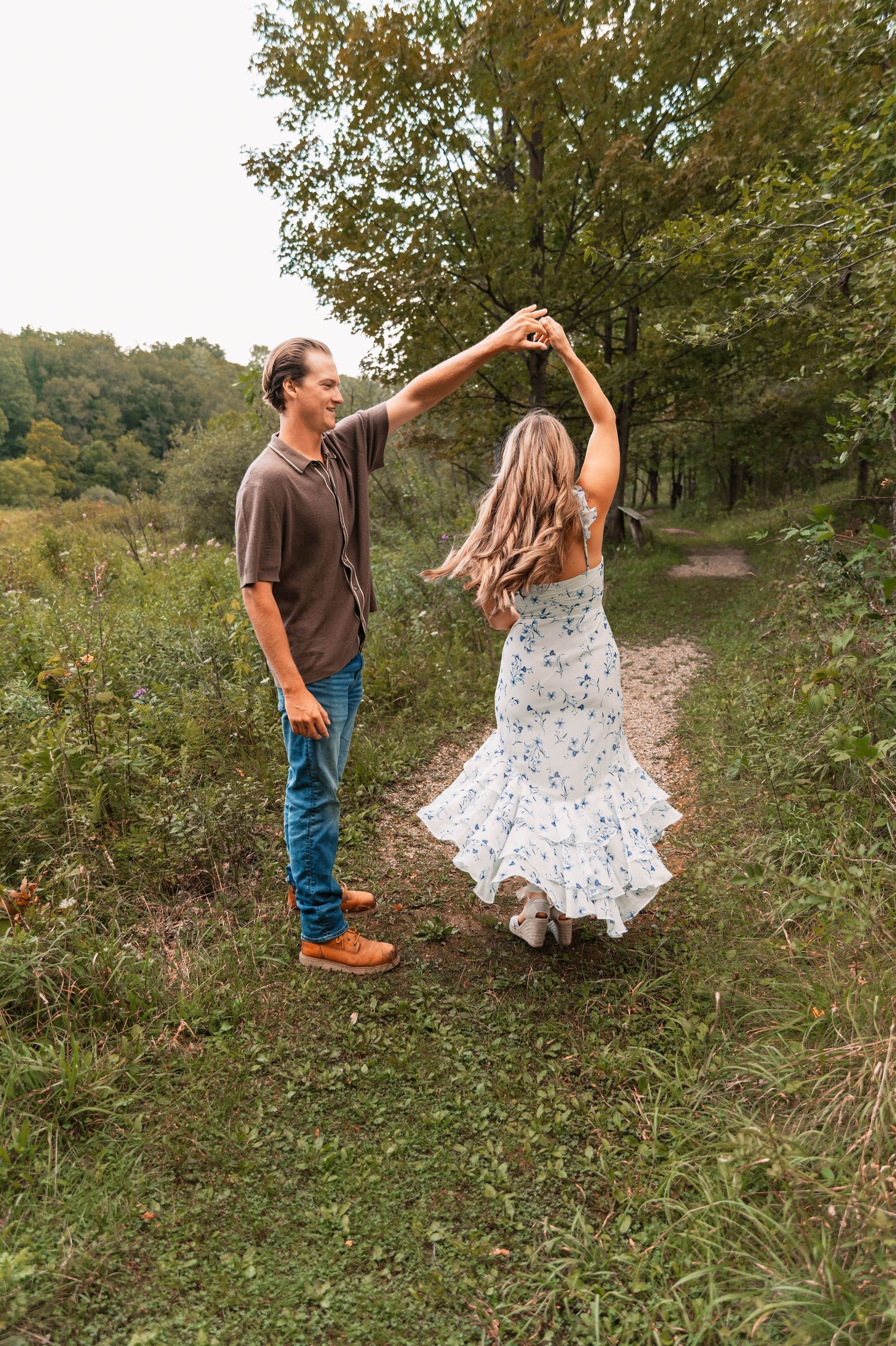 A couple dances playfully in a grassy field during autumn.