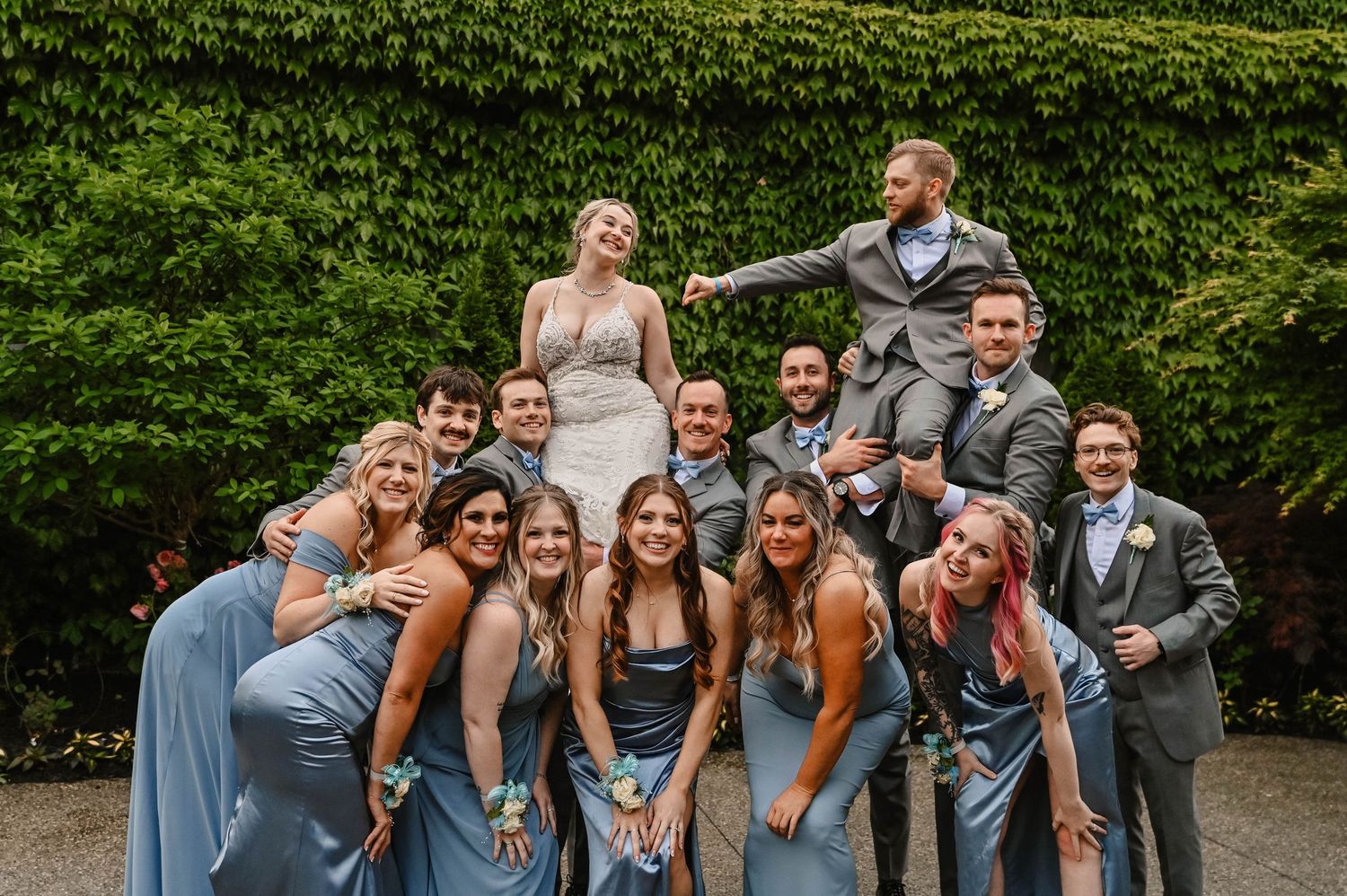 Wedding party poses playfully on steps covered in ivy for group photo.