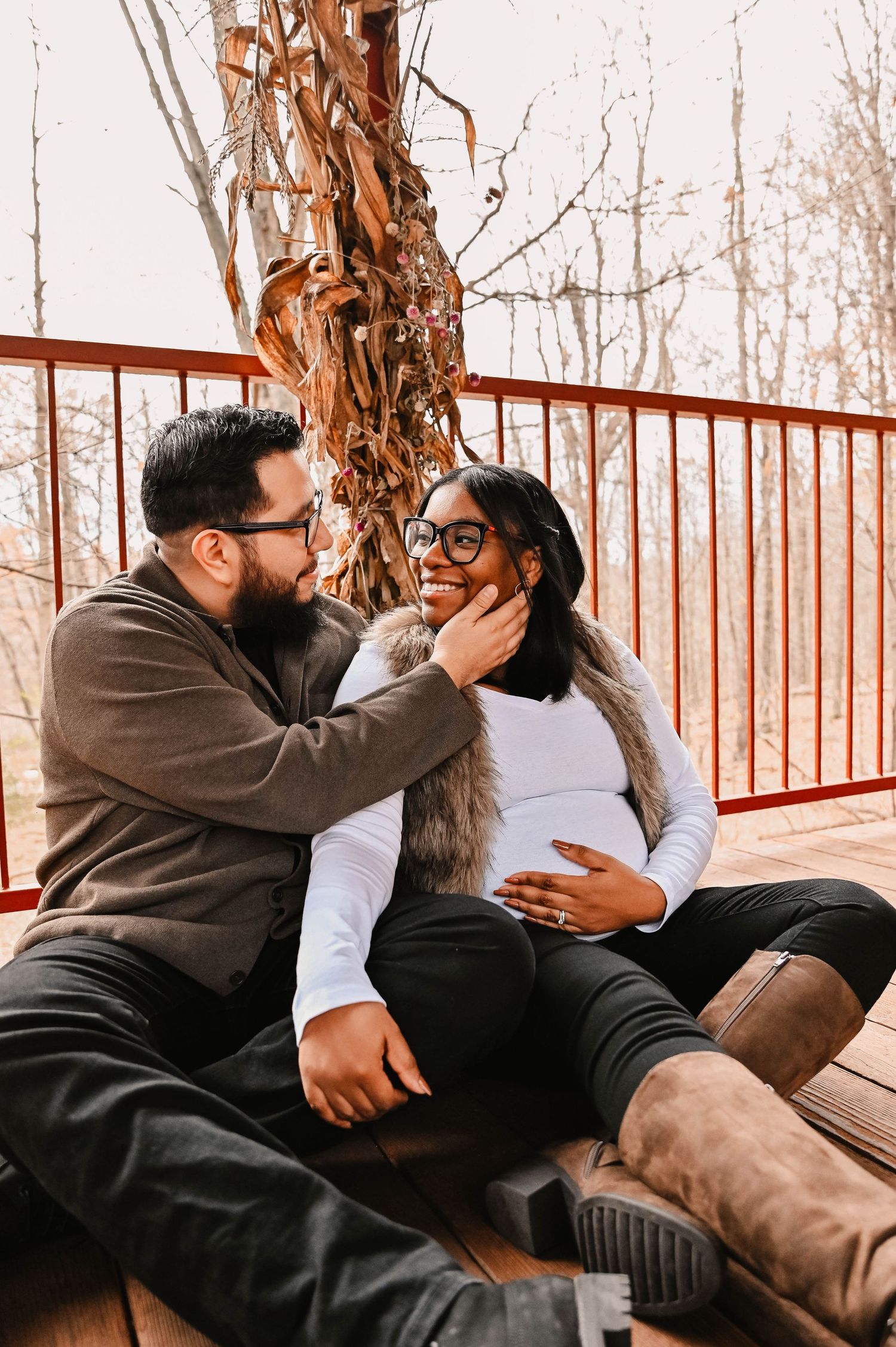 A couple shares a tender moment on a wooden deck surrounded by autumn trees.