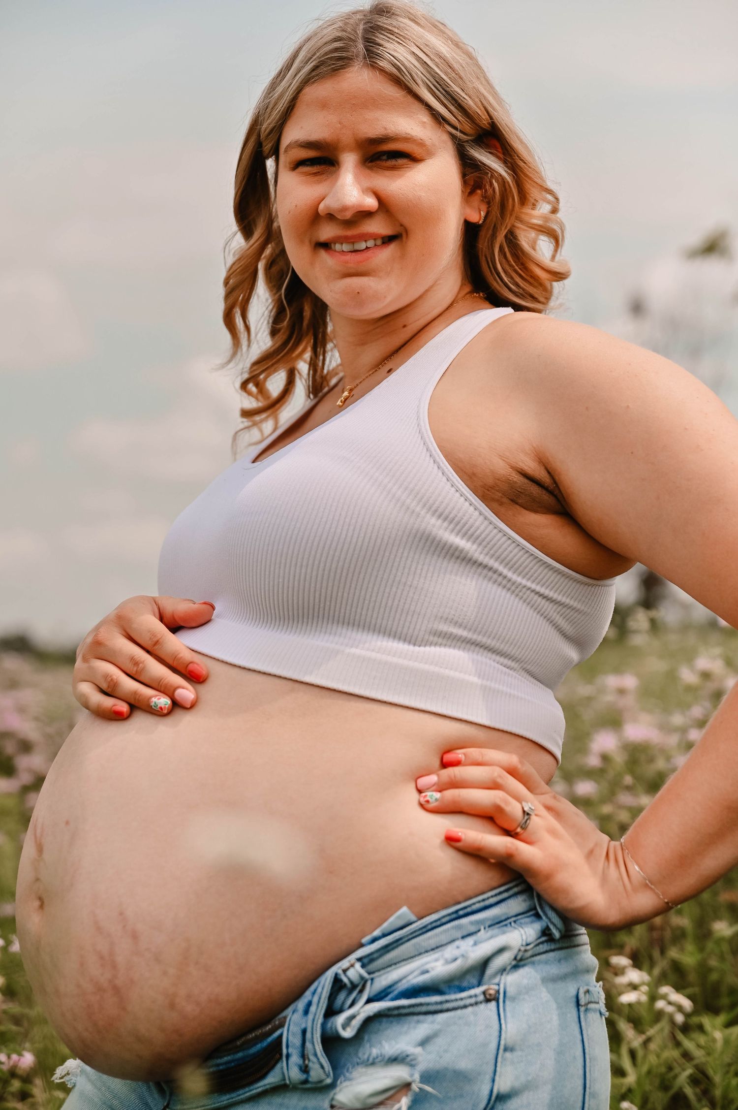 Close-up shots of a pregnant belly in a white tank top and jeans against a natural outdoor backdrop.