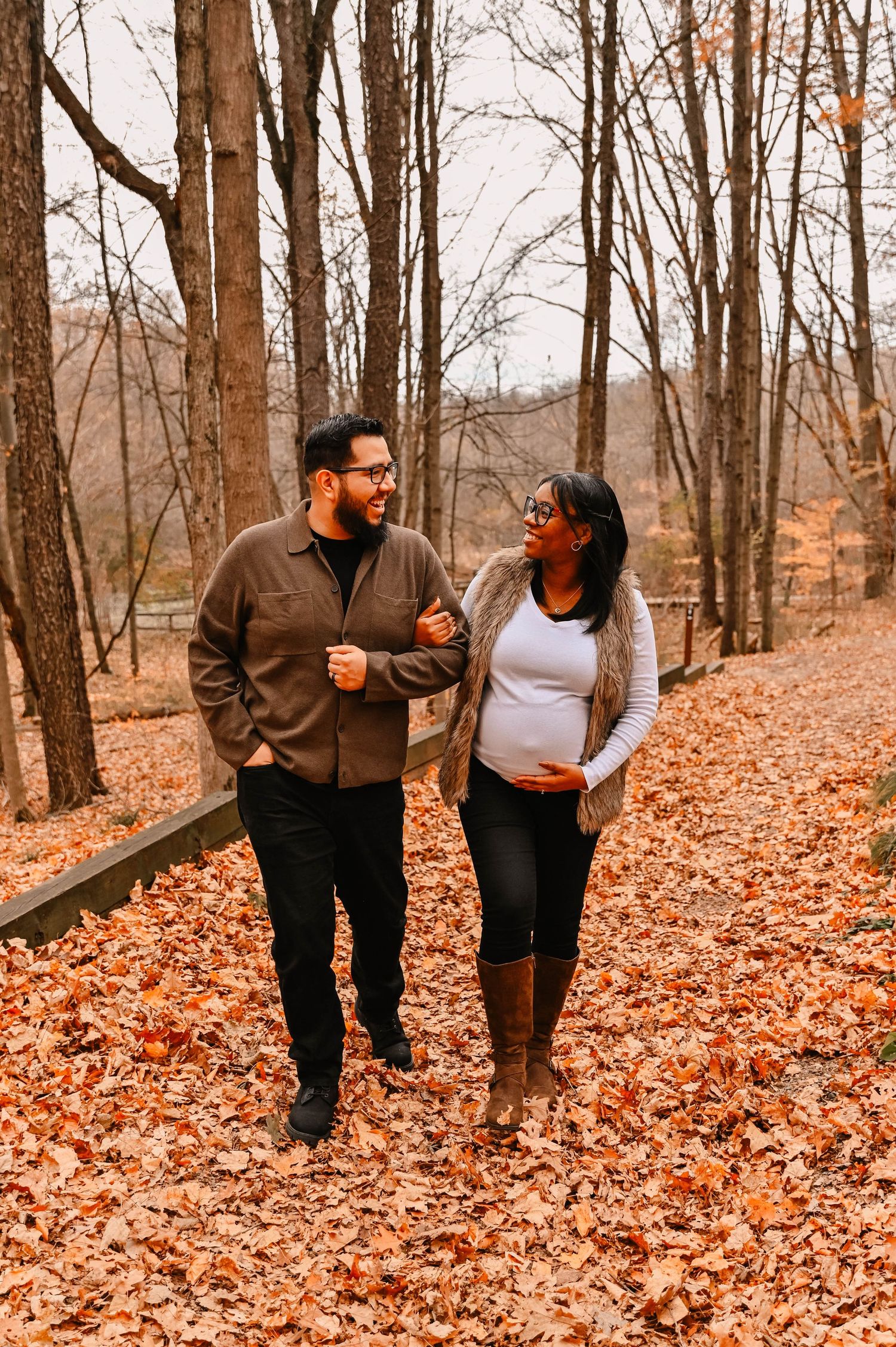 A couple walks through autumn leaves in a wooded area.
