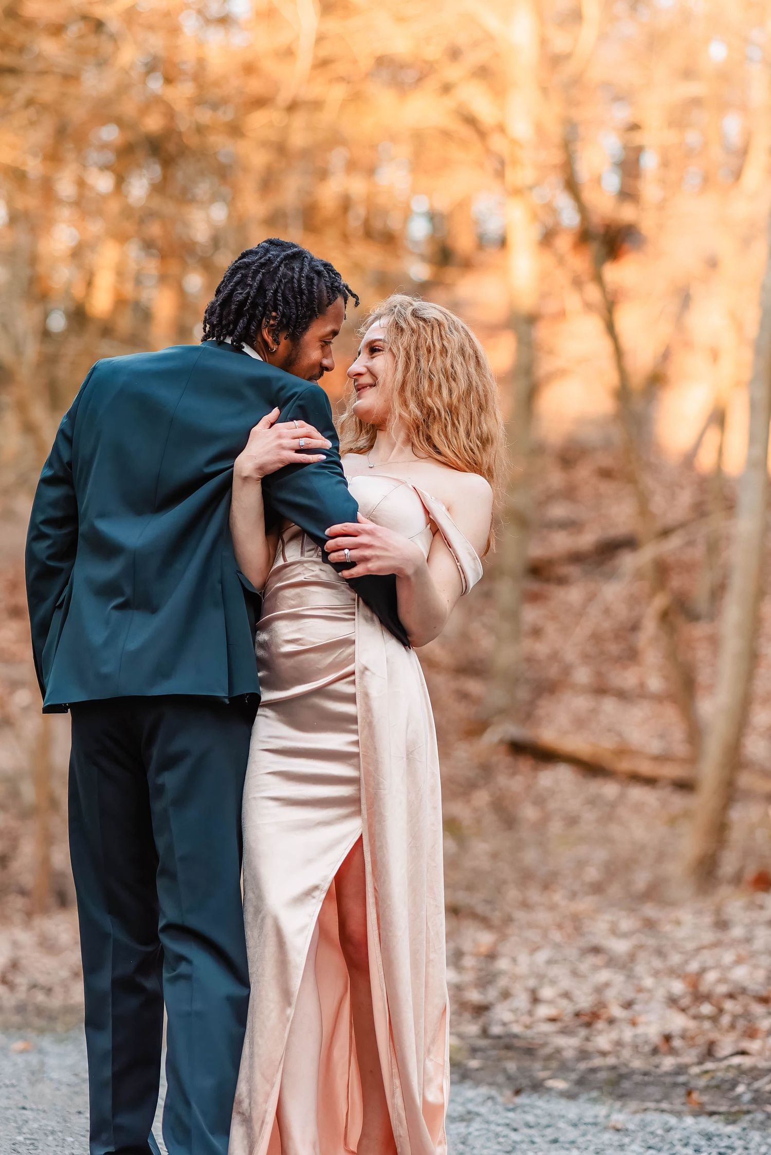 A couple in formal attire embracing in an autumn forest setting.