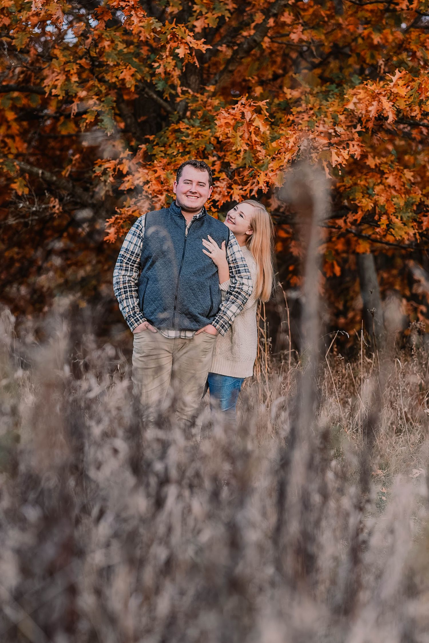 Romantic autumn engagement photos with orange fall foliage and tall grass in the background.