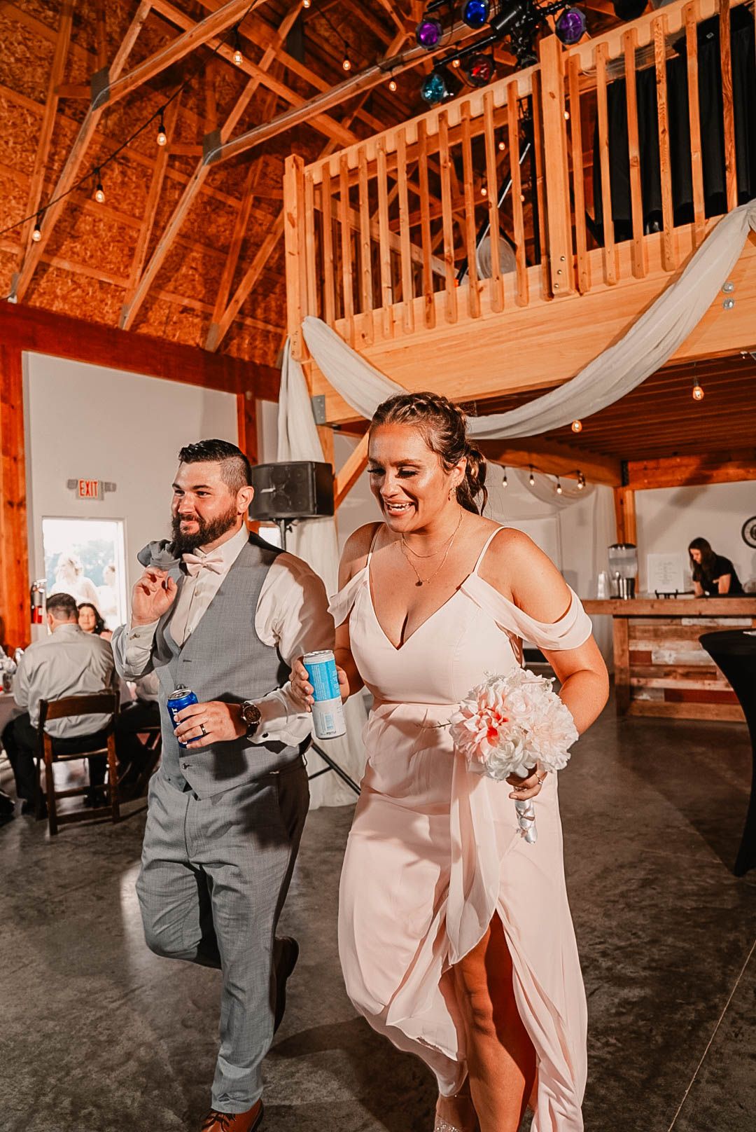 Wedding party members dancing and celebrating inside a wooden barn reception venue.