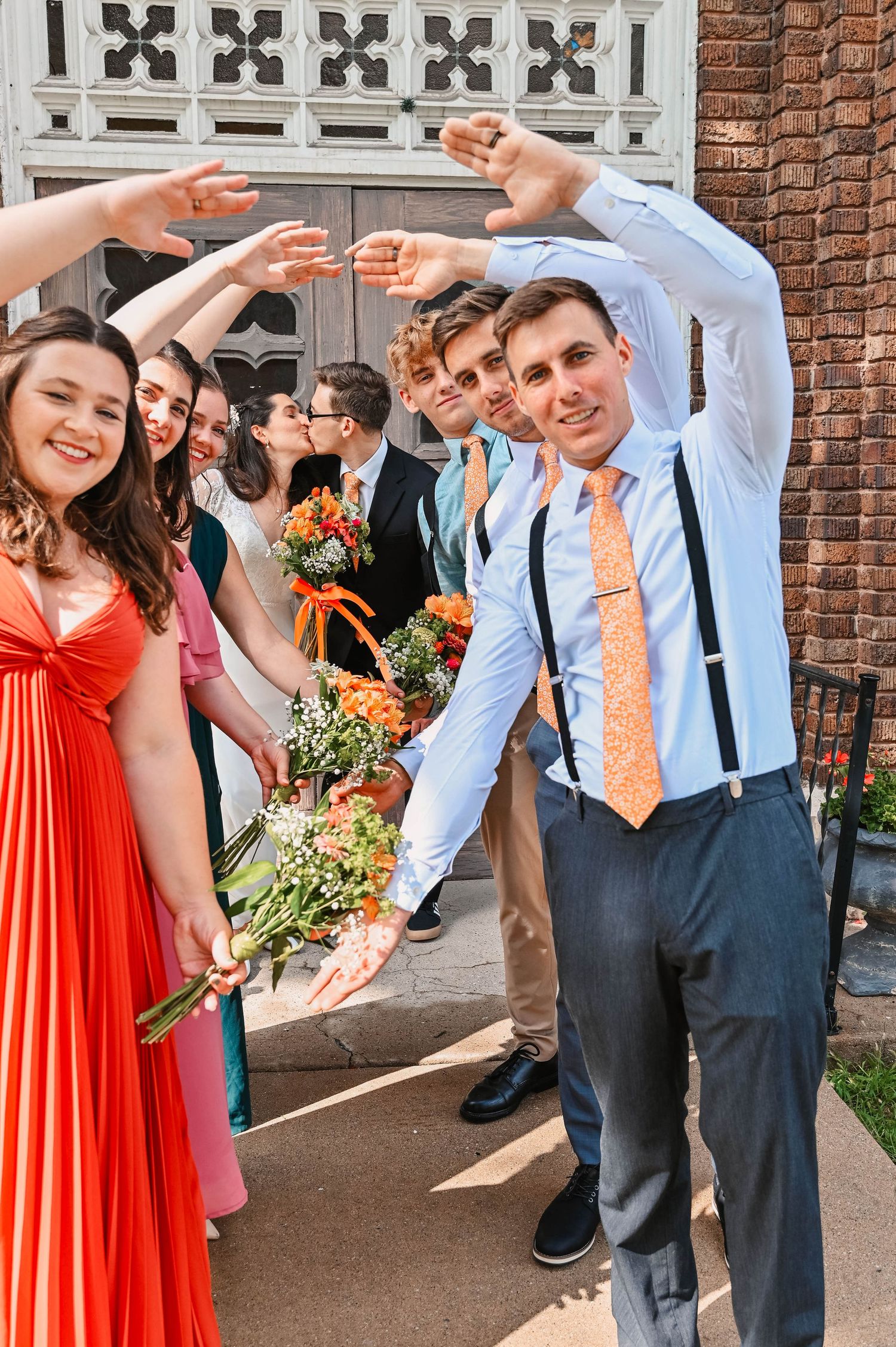 Wedding party dancing and celebrating on church steps with colorful attire and flowers.