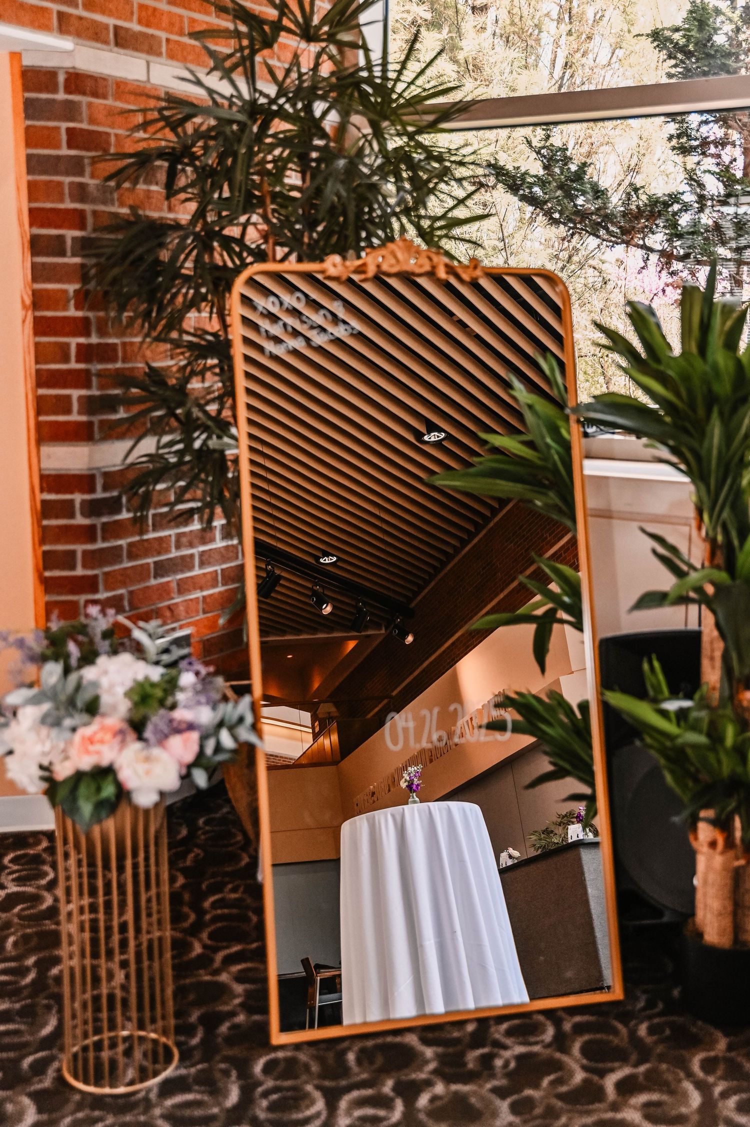 Modern copper-framed mirror with plants and floral arrangements in an interior setting.