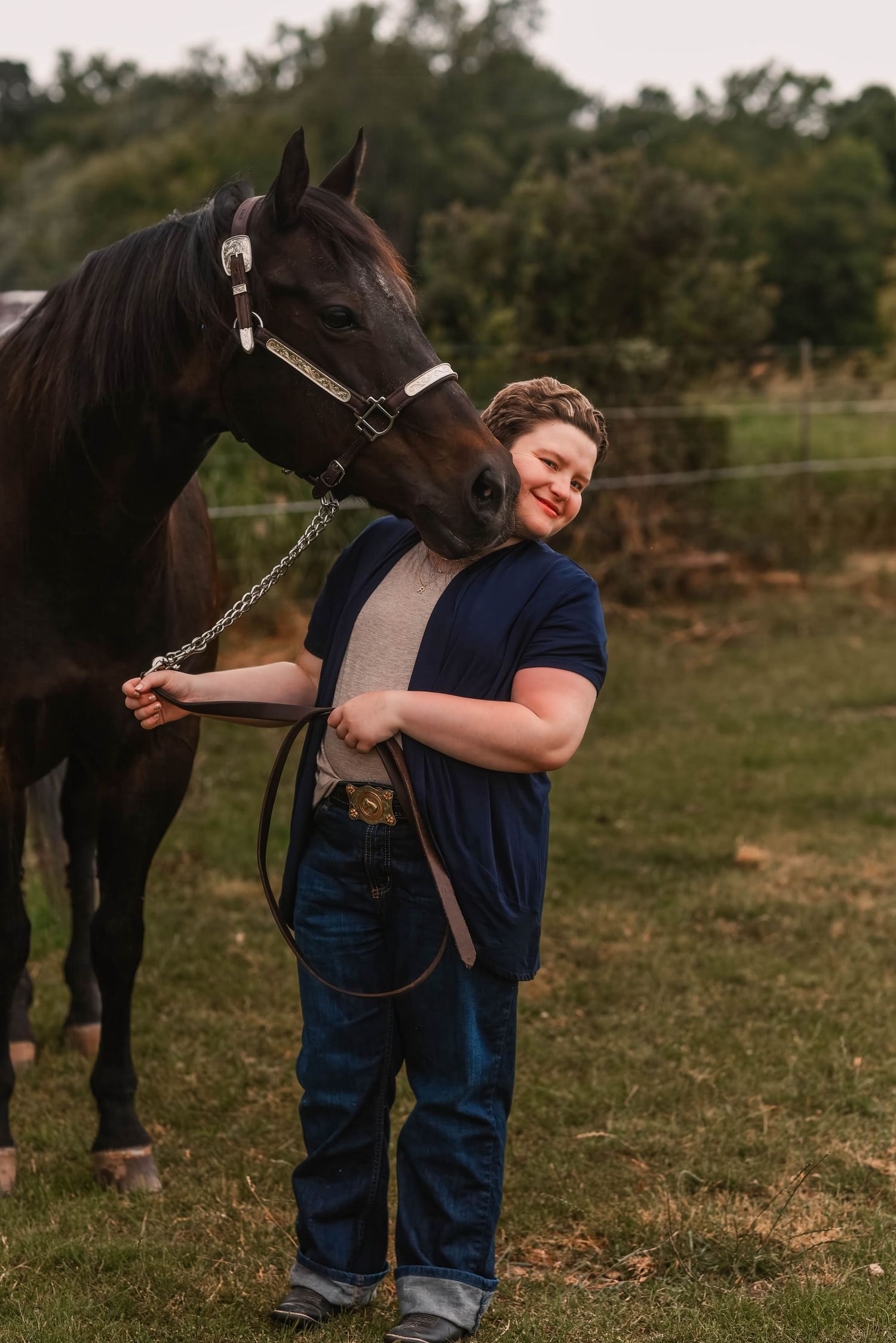 Young person sharing a tender moment with a black horse in a pastoral setting.