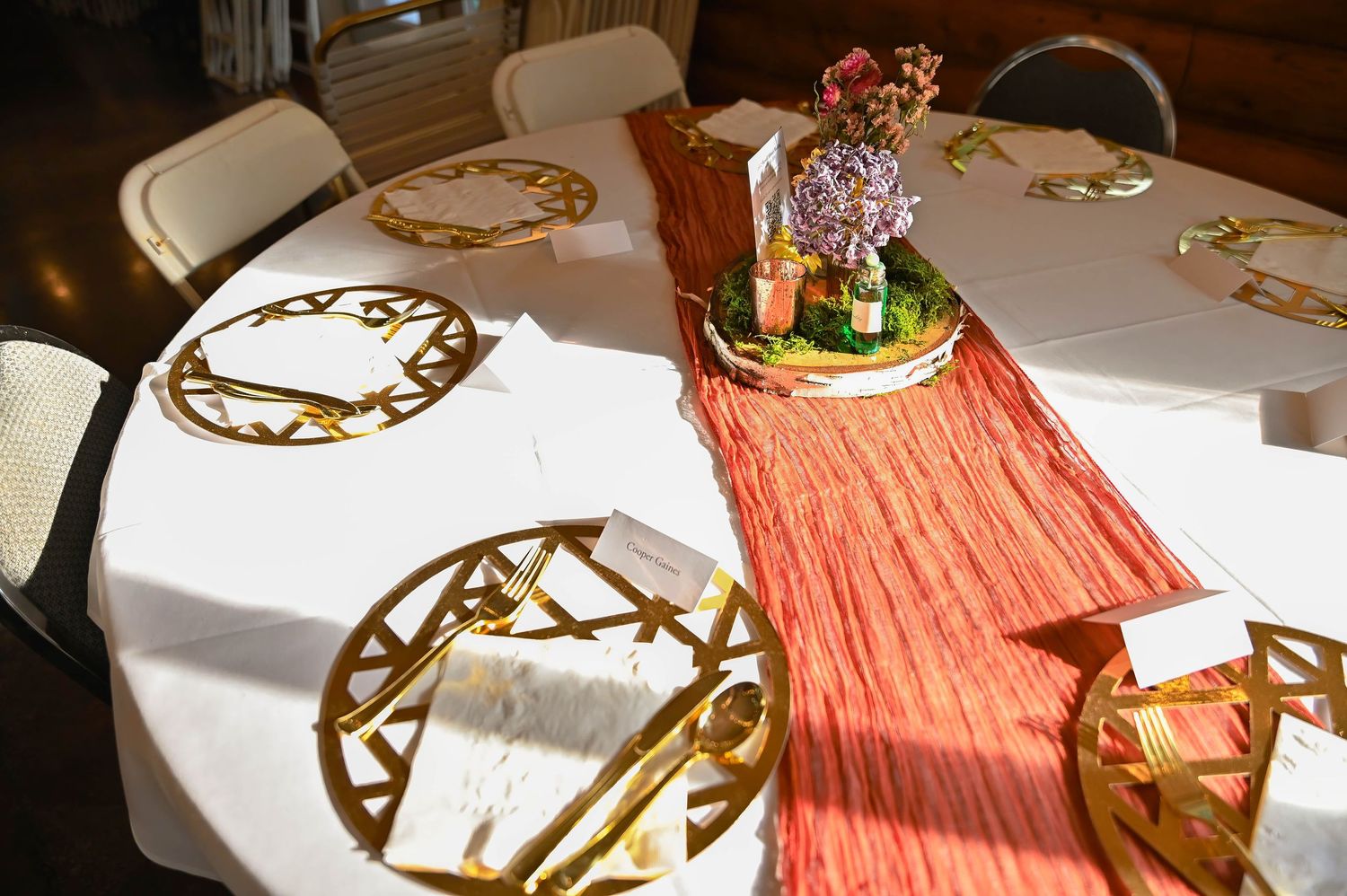 Wedding reception table setting with gold charger plates and coral table runner.