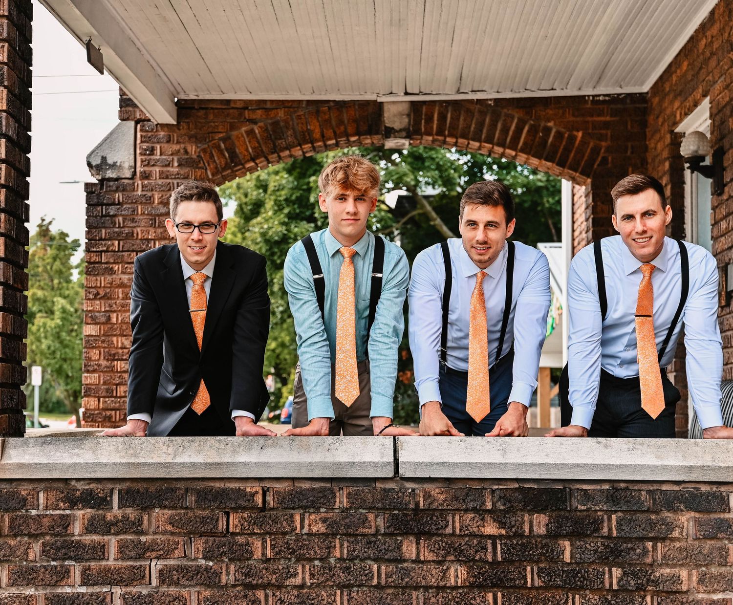 Groomsmen pose under covered porch of brick building.