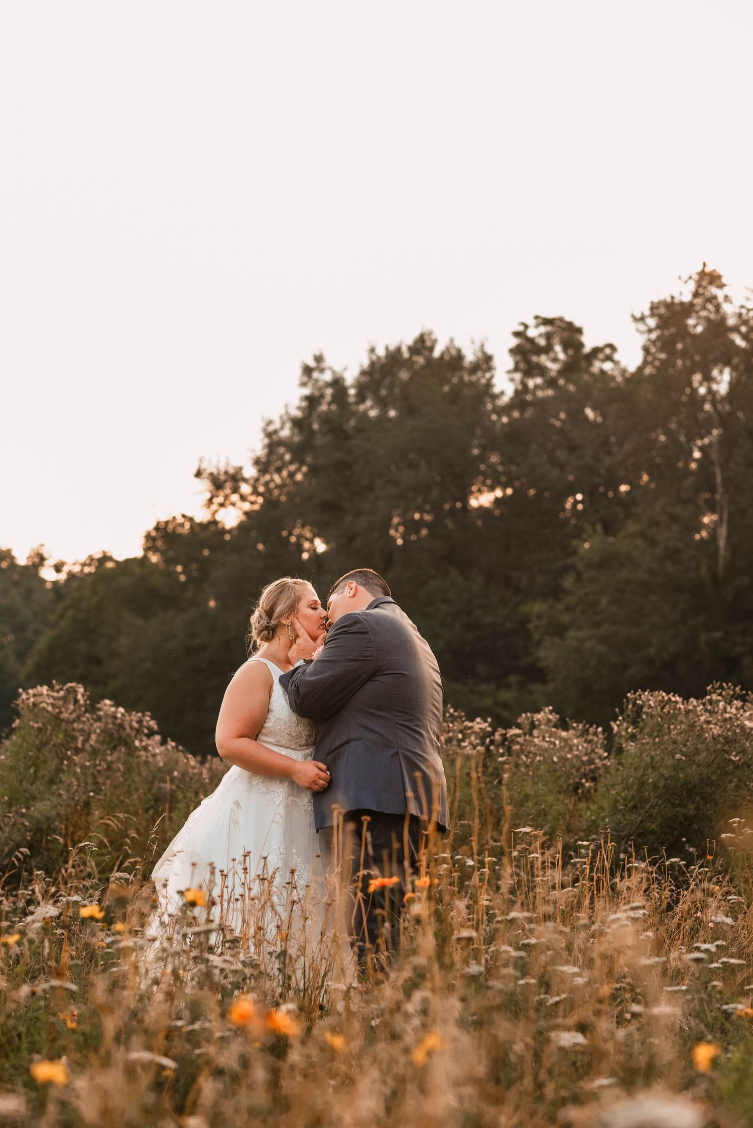 Newlyweds embrace in a golden sunlit wildflower field at sunset.