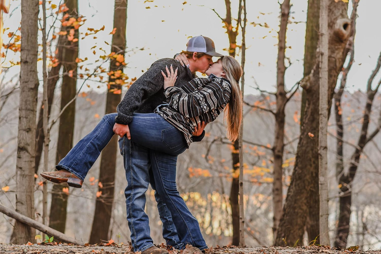 Romantic autumn engagement photos with couple in casual attire among trees.