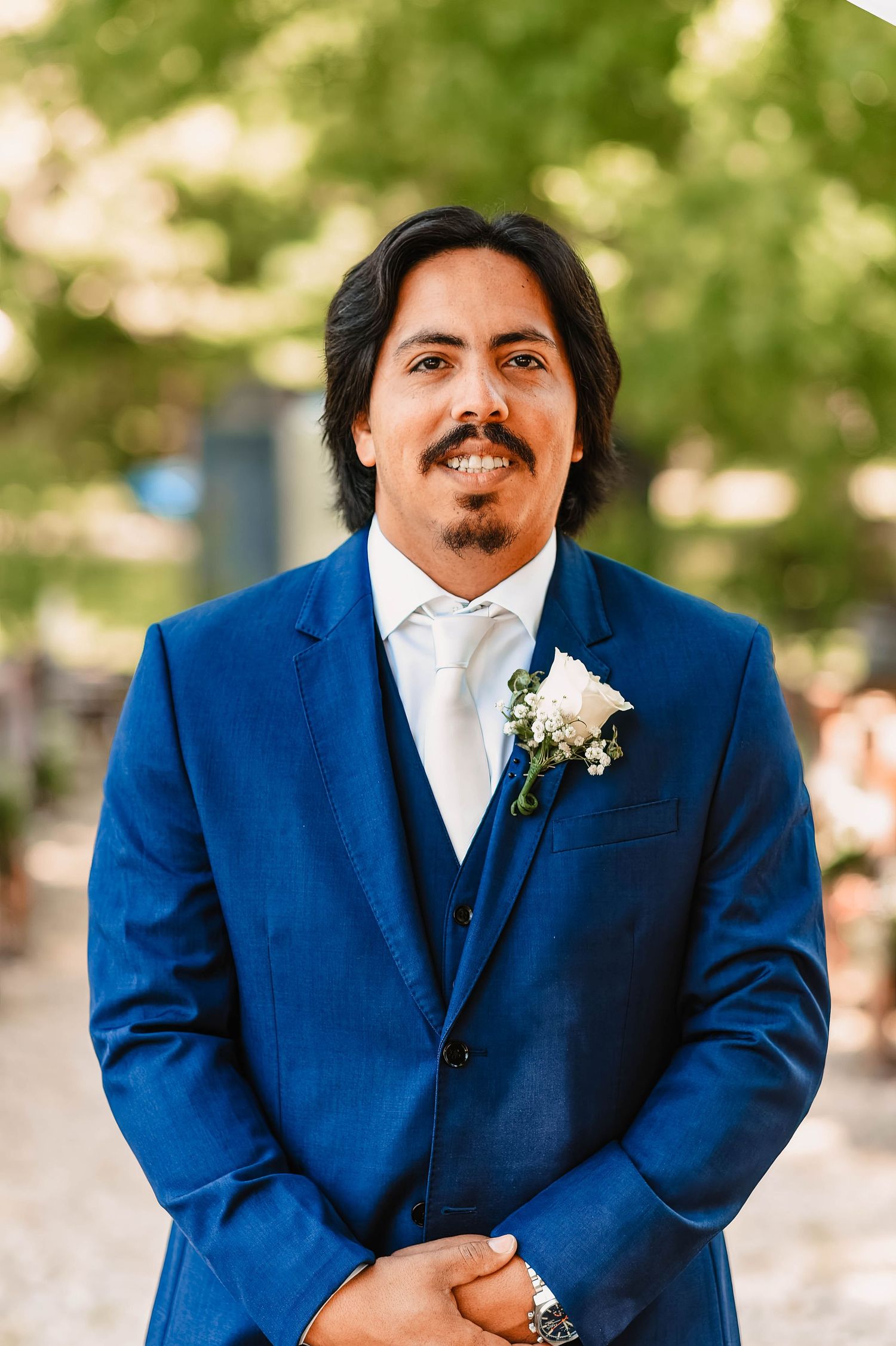A person in a royal blue suit and white boutonniere poses for formal wedding photos.