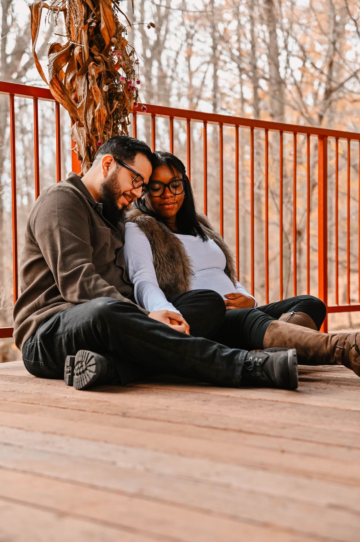 A couple relaxes together on a wooden deck during an autumn photoshoot.