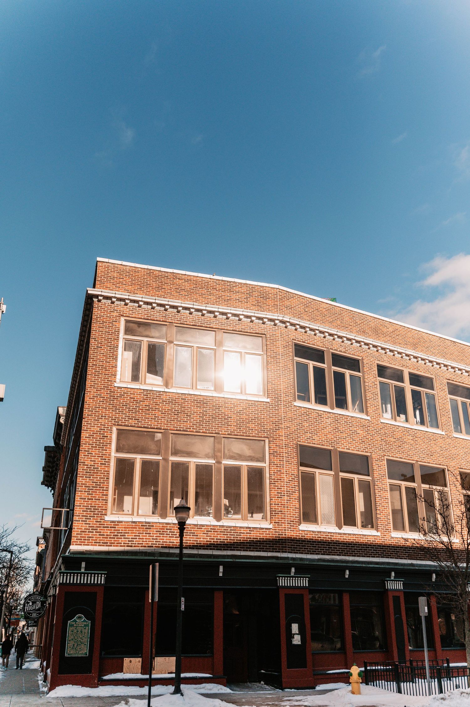 A panoramic view of a vintage brick commercial building with large windows under blue sky.