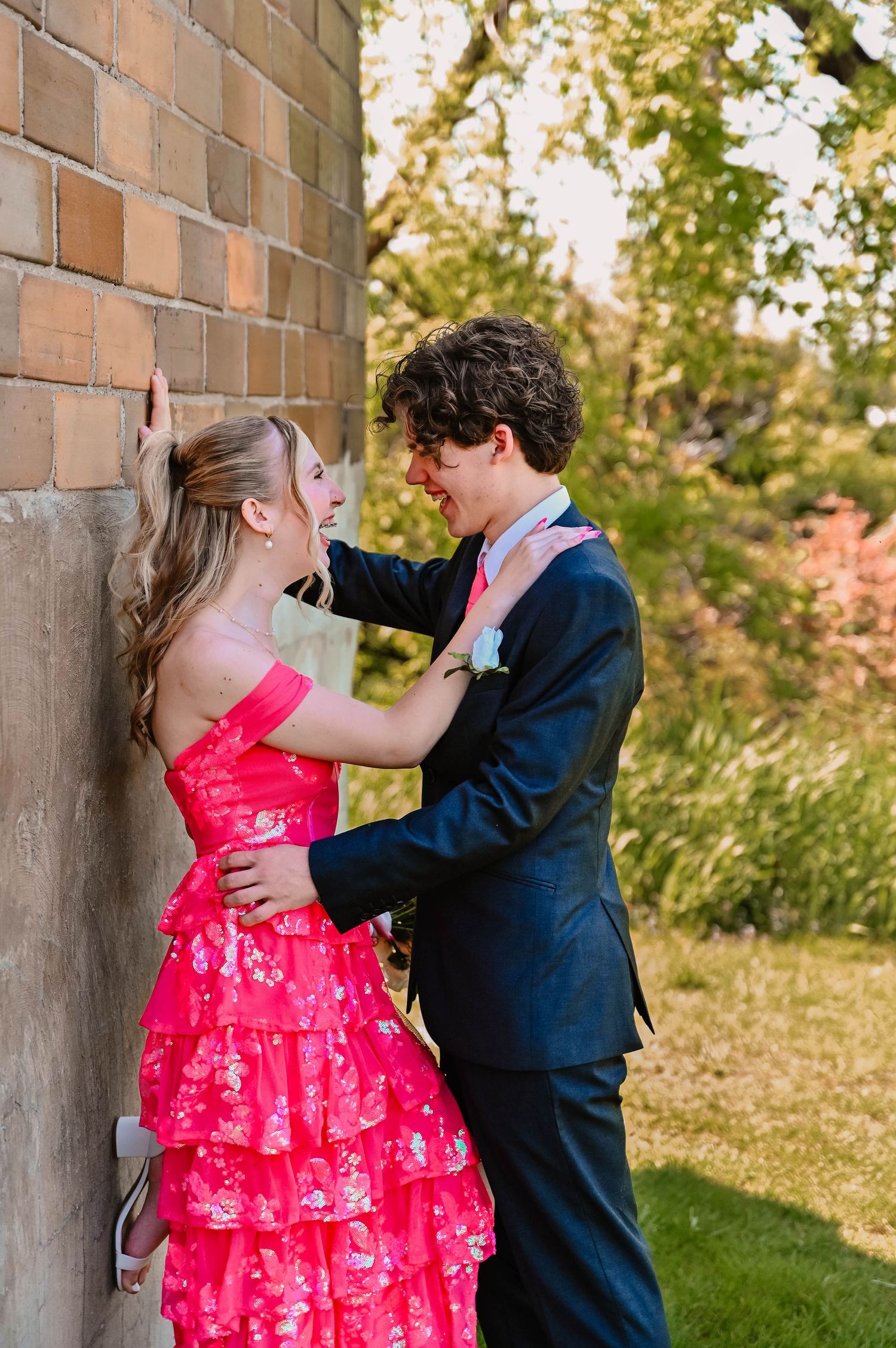 A couple dances and embraces near a brick wall outdoors.