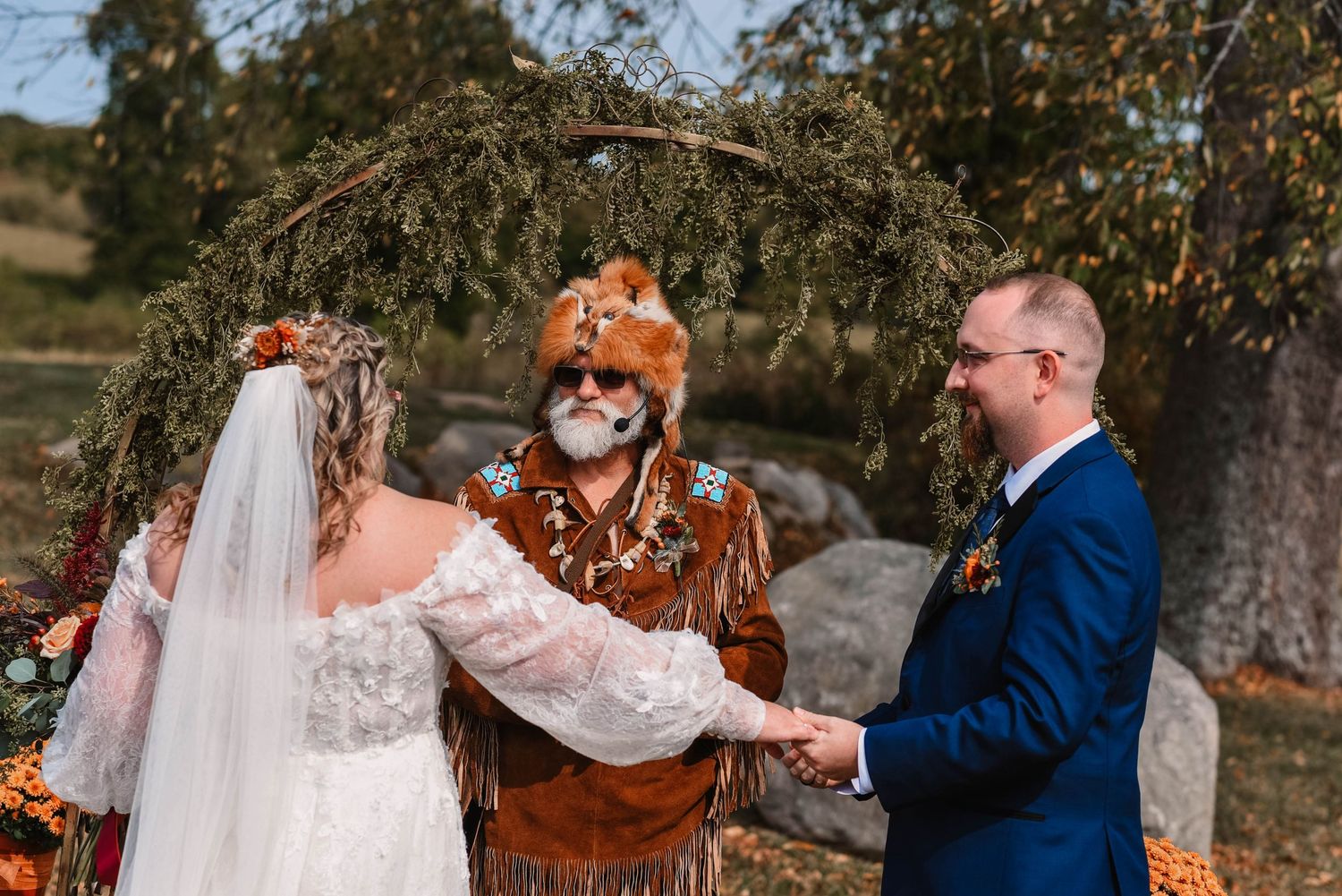 Outdoor wedding ceremony under rustic arch with officiant in fox costume.