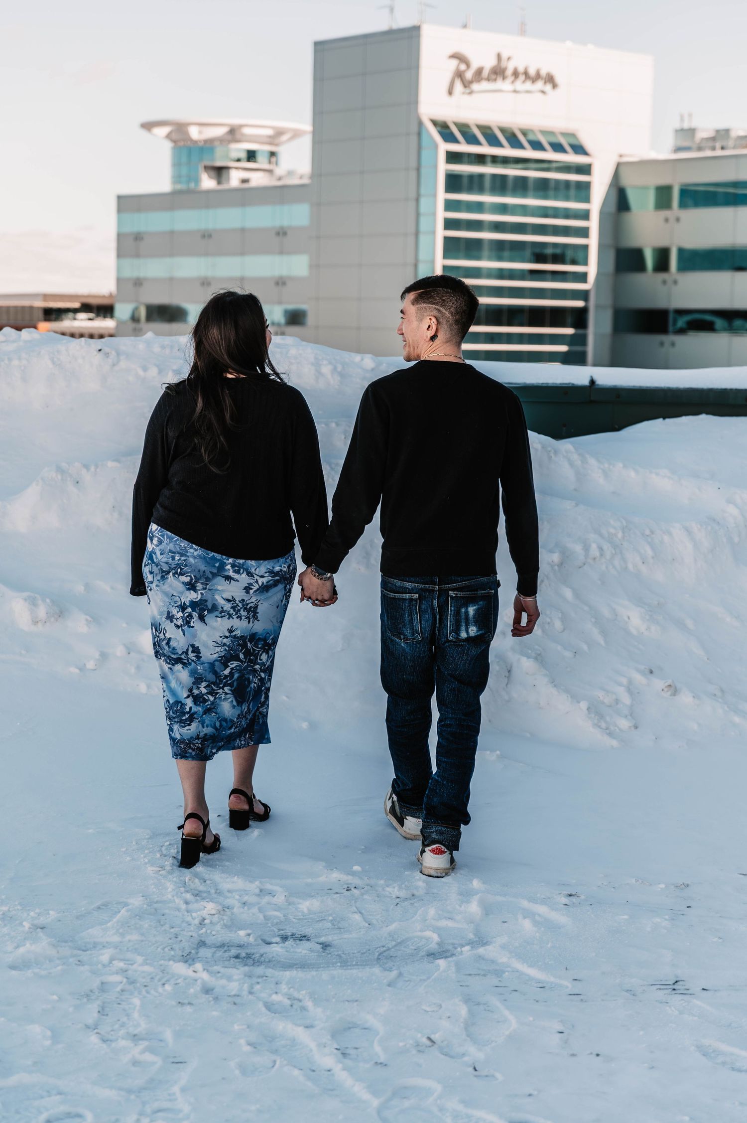 Couple walking hand in hand through snowy winter landscape.