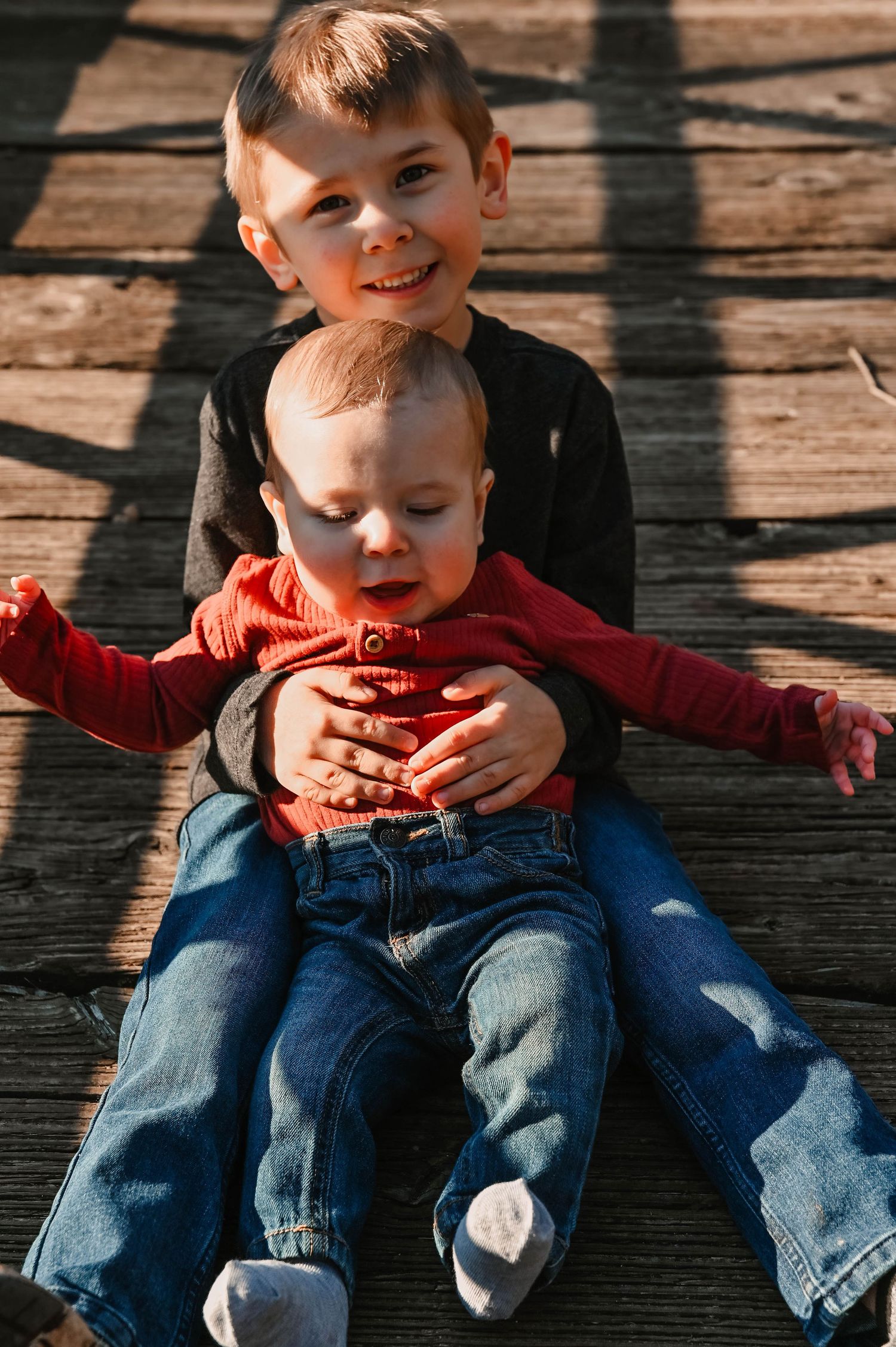 Two siblings share a sweet moment on wooden decking in casual denim outfits.