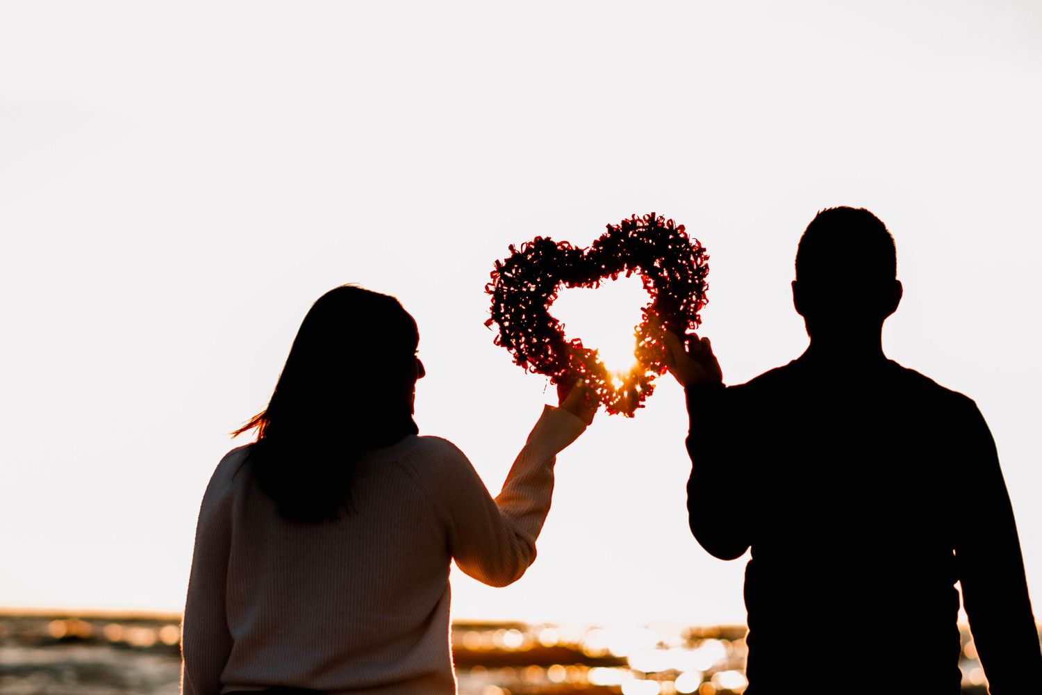 Silhouettes of a couple sharing a romantic moment at sunset against an orange sky.