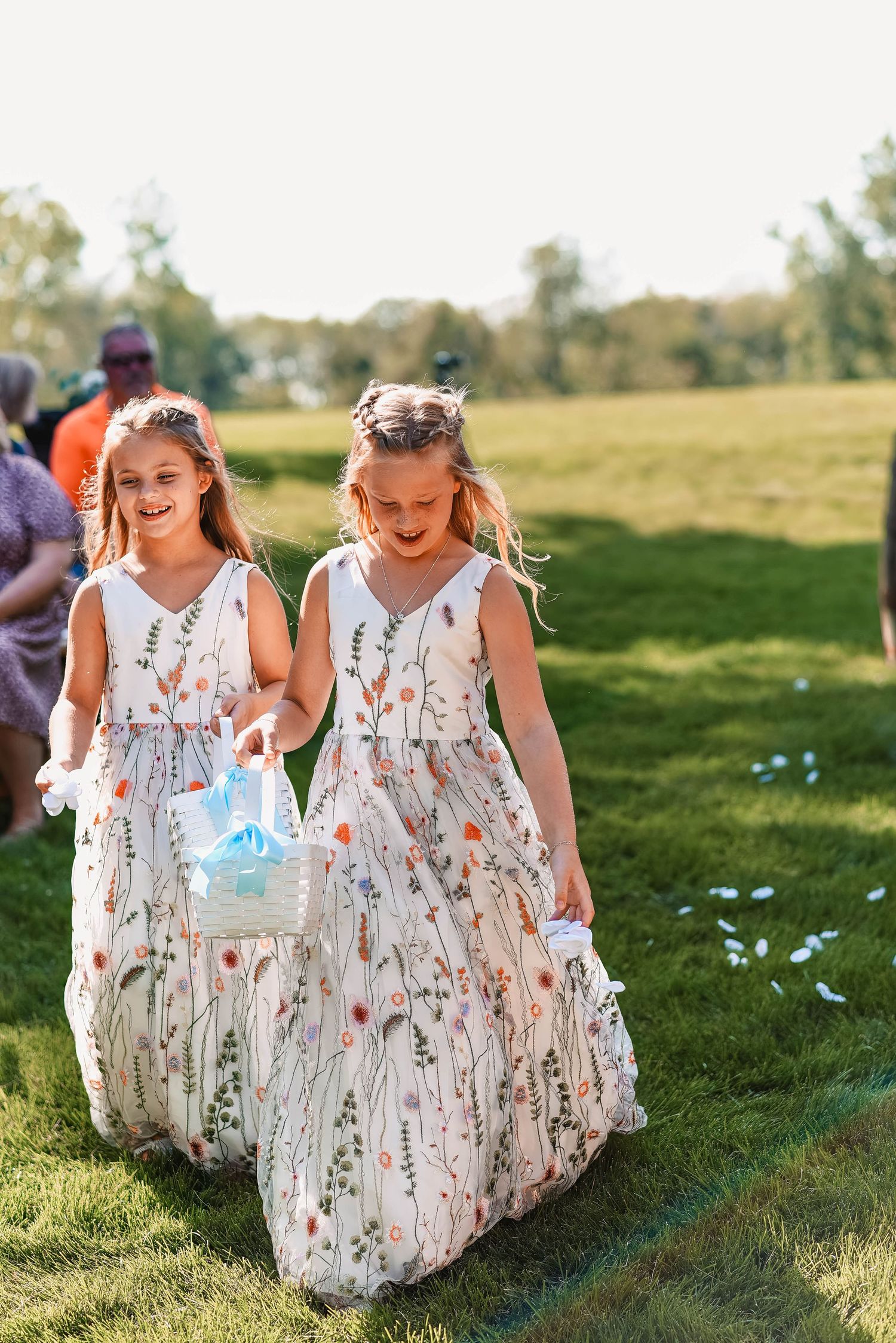 Young flower girls in floral dresses run playfully through a sunny meadow.