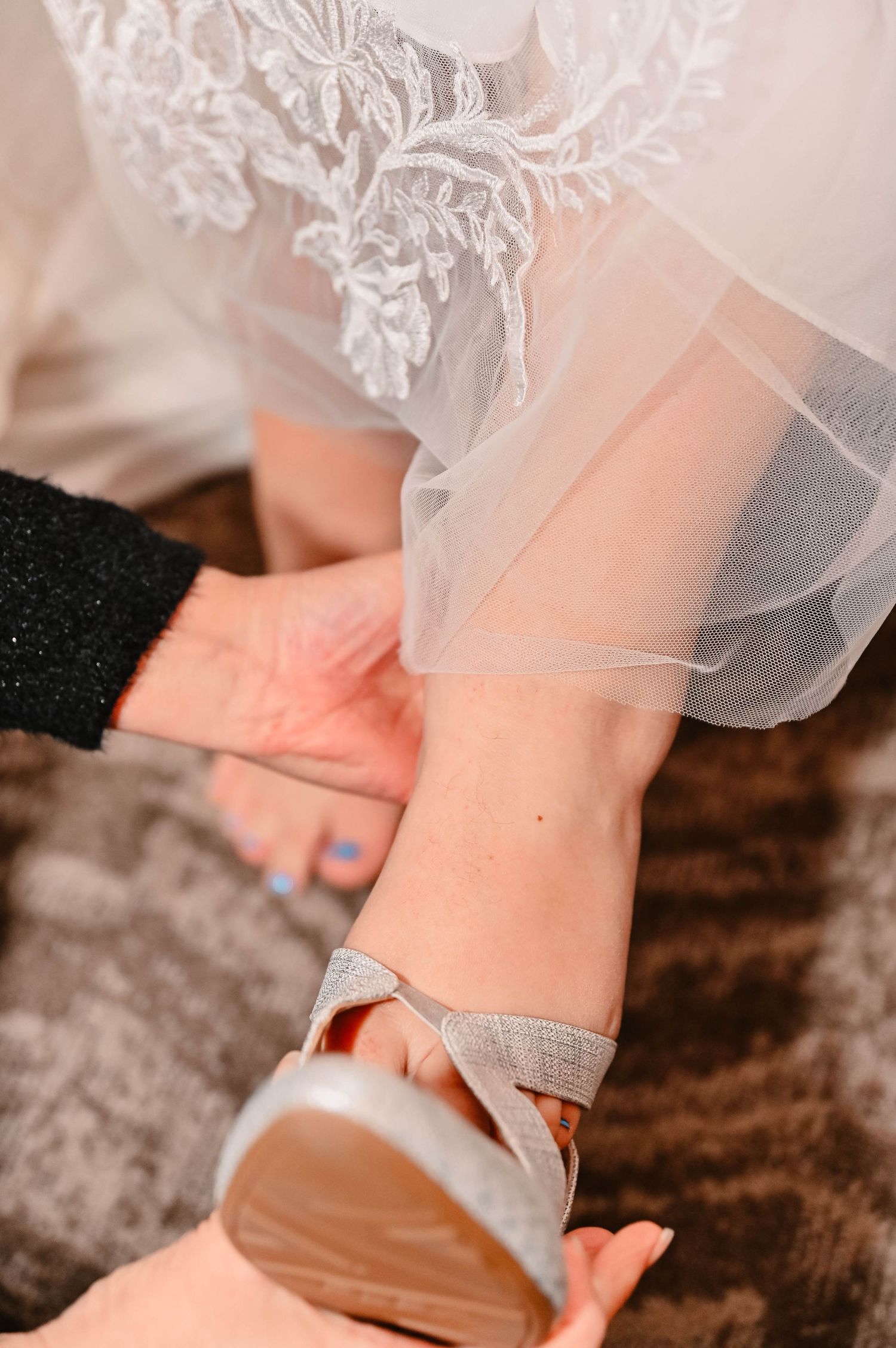 Close-up of sparkly silver wedding shoes peeking out from under a white lace dress hem.