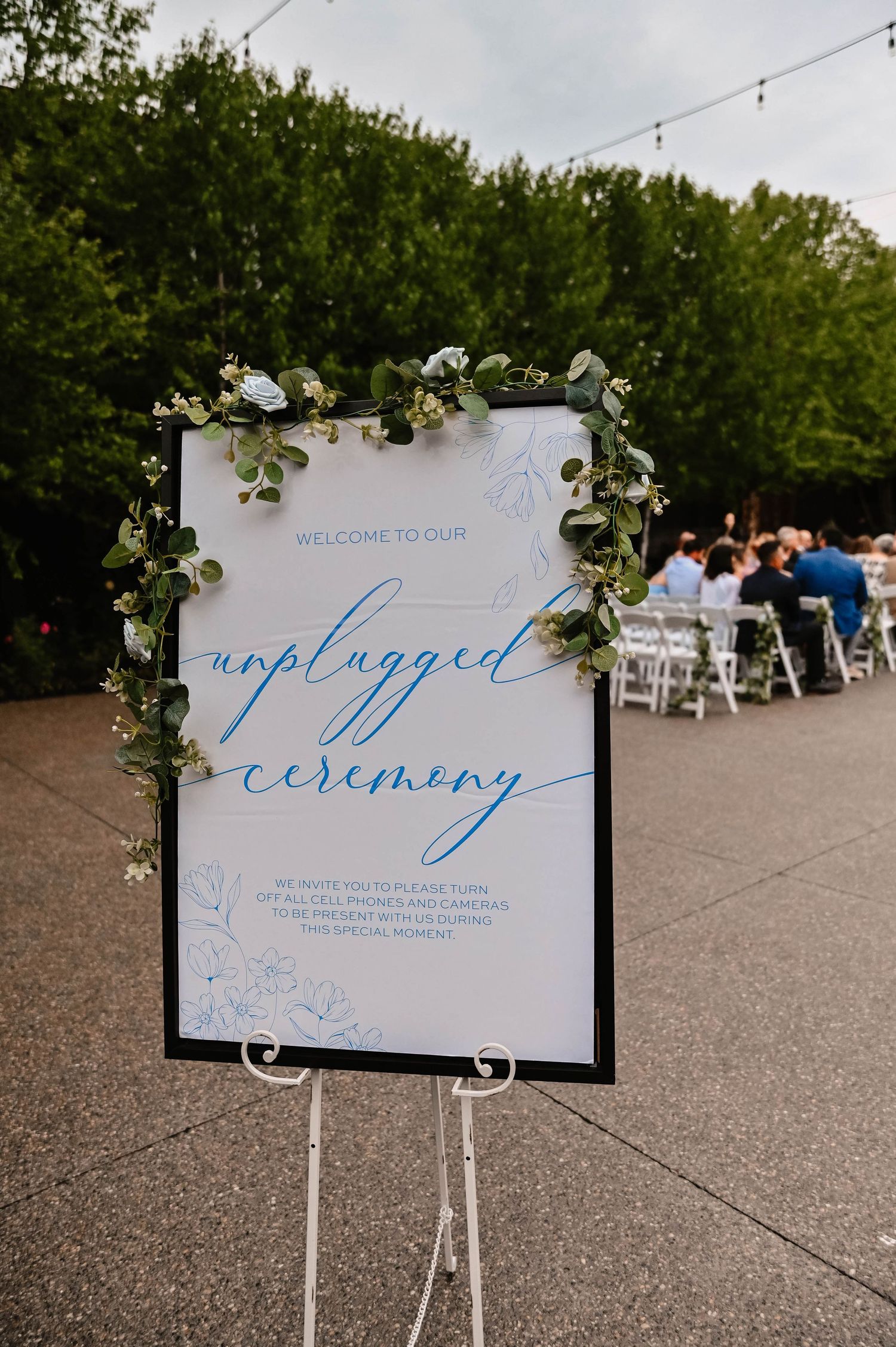 Elegant wedding ceremony welcome sign with blue calligraphy and floral decorations.