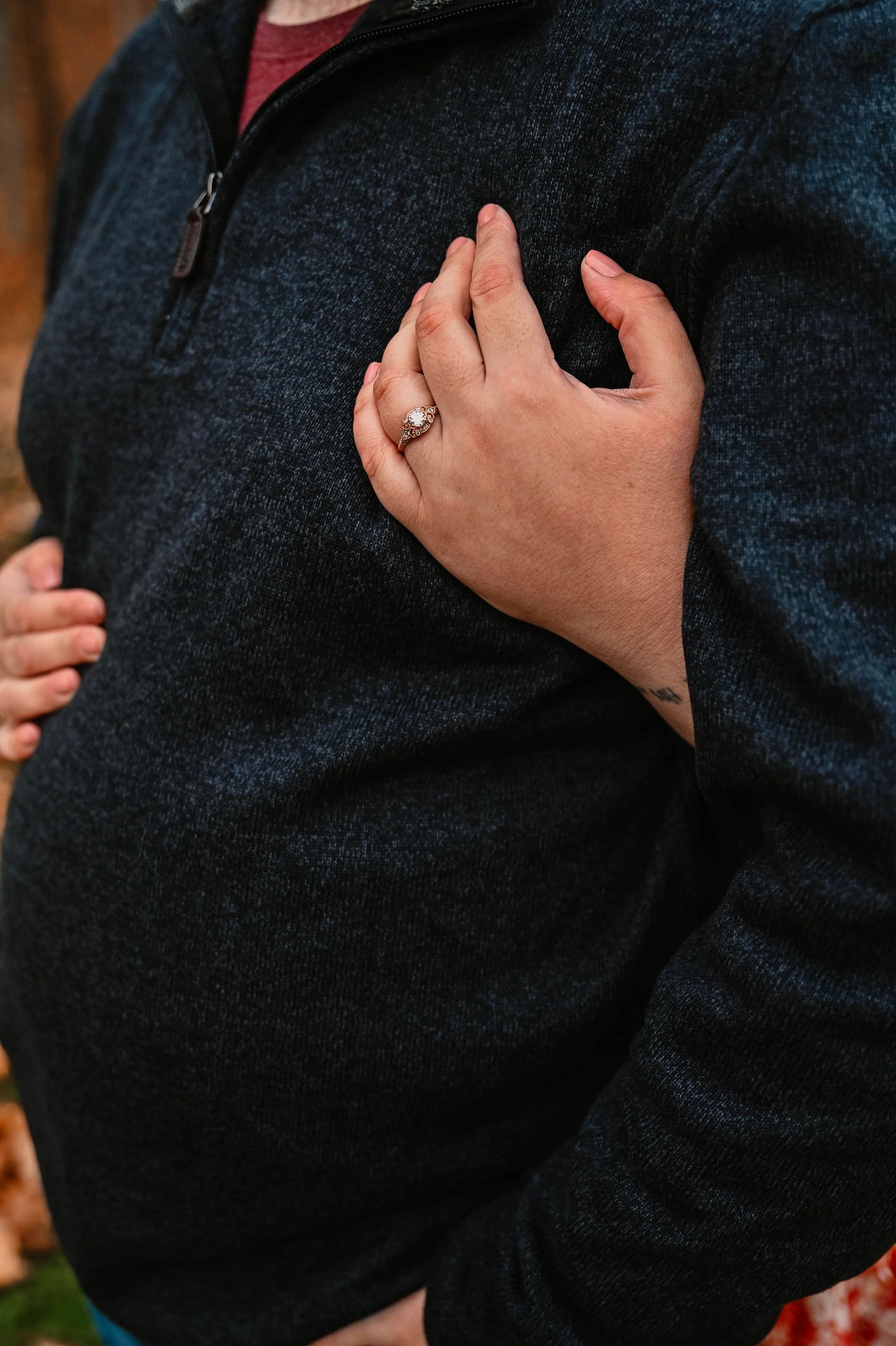 Detail shot of engagement ring against dark sweater during autumn photoshoot.