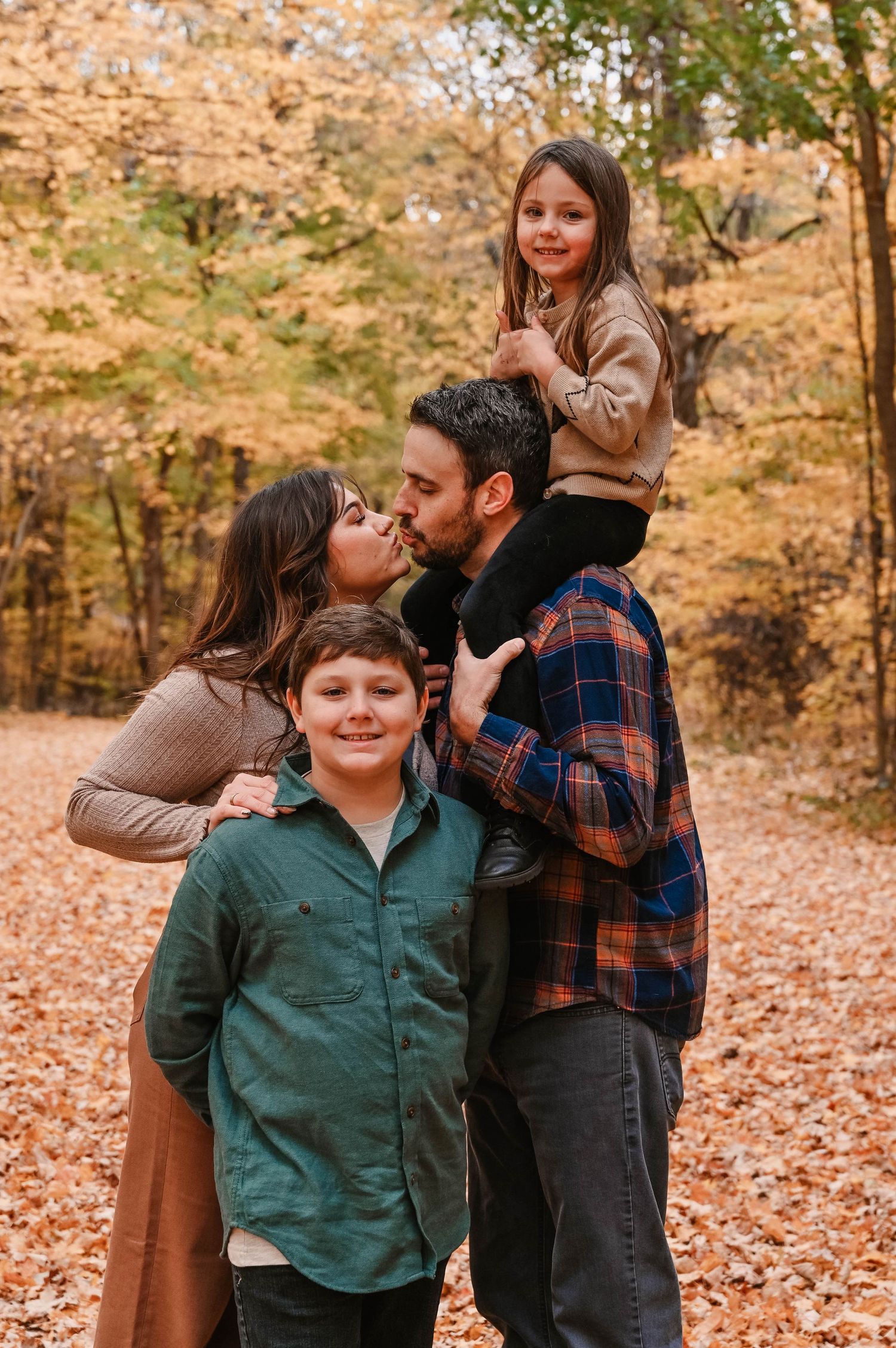 A joyful family portrait captured in a forest filled with golden autumn leaves.