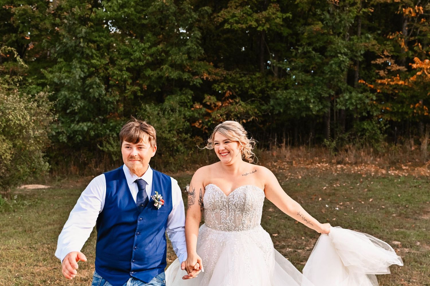 Newlyweds walking through an autumn field in casual wedding attire.
