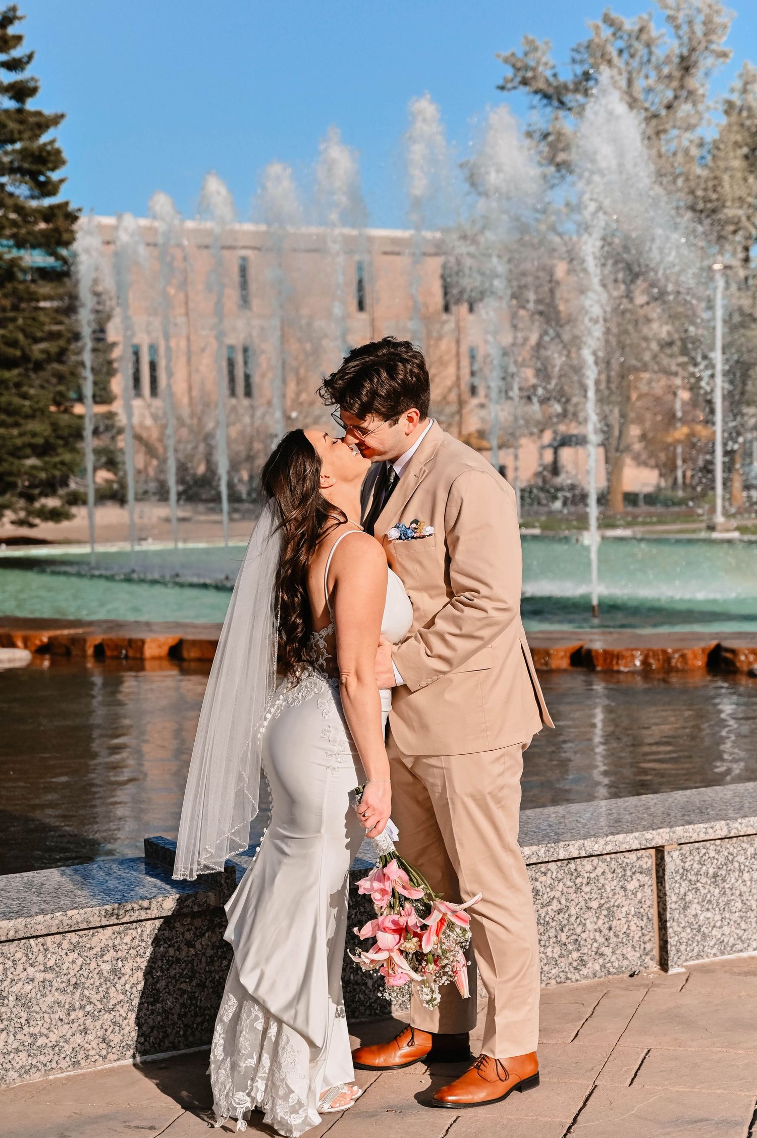 Romantic couple sharing a moment by a fountain with brick building in background.