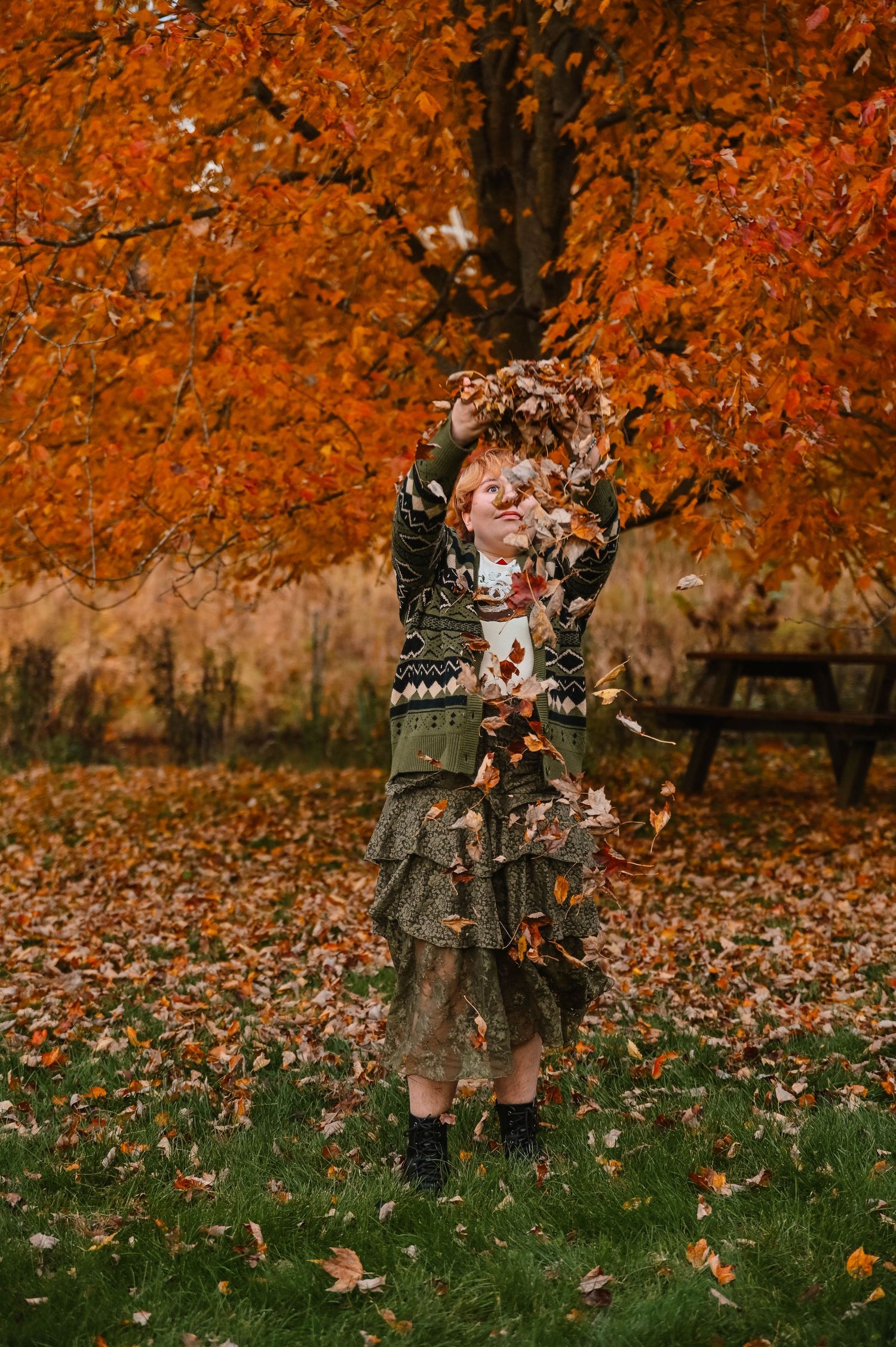 Figure stands among falling autumn leaves in a park setting.